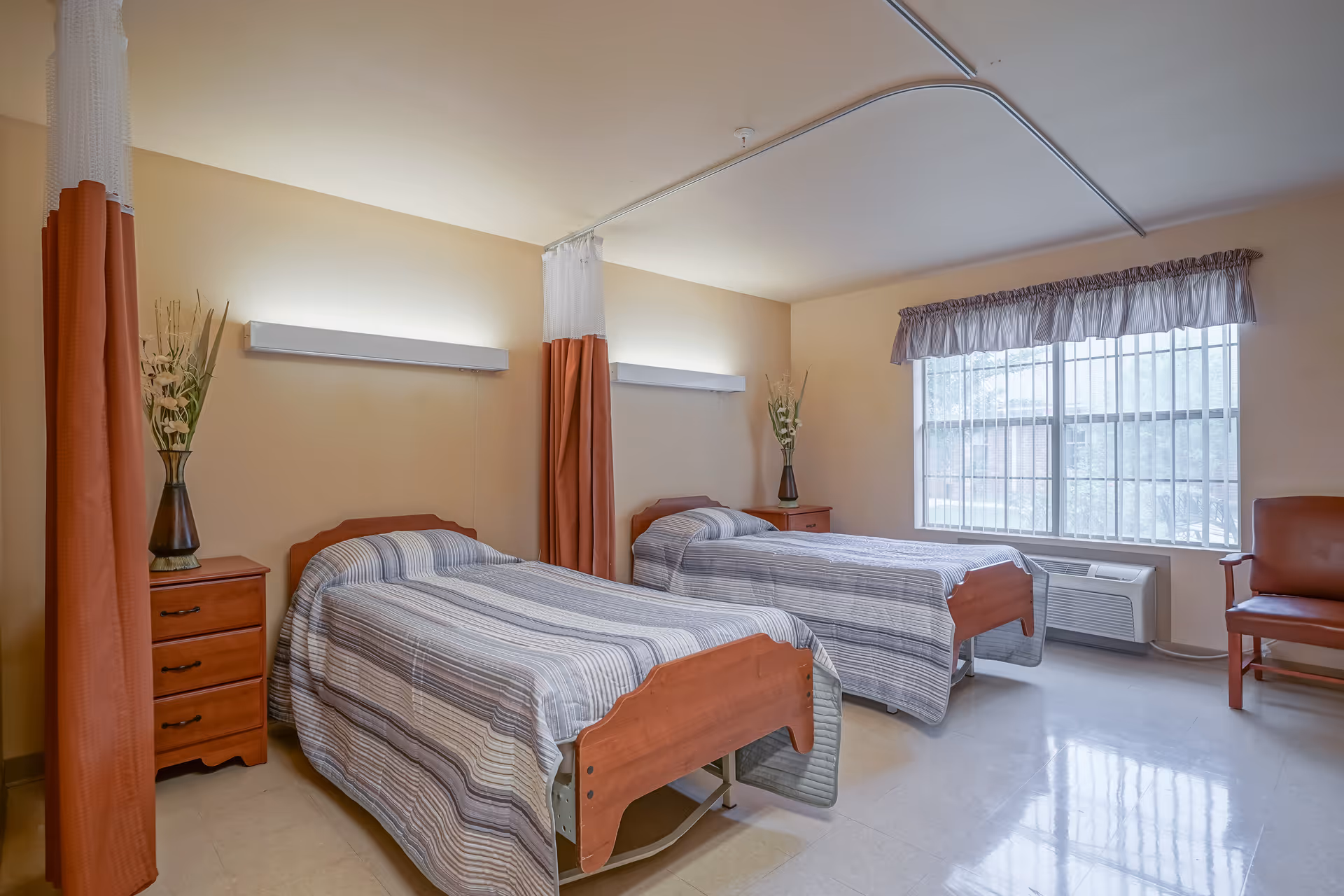A bright shared bedroom with two single beds, wooden nightstands, privacy curtains, and a window letting in natural light.