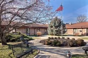 Exterior view of a brick senior living center with flagpole and benches.