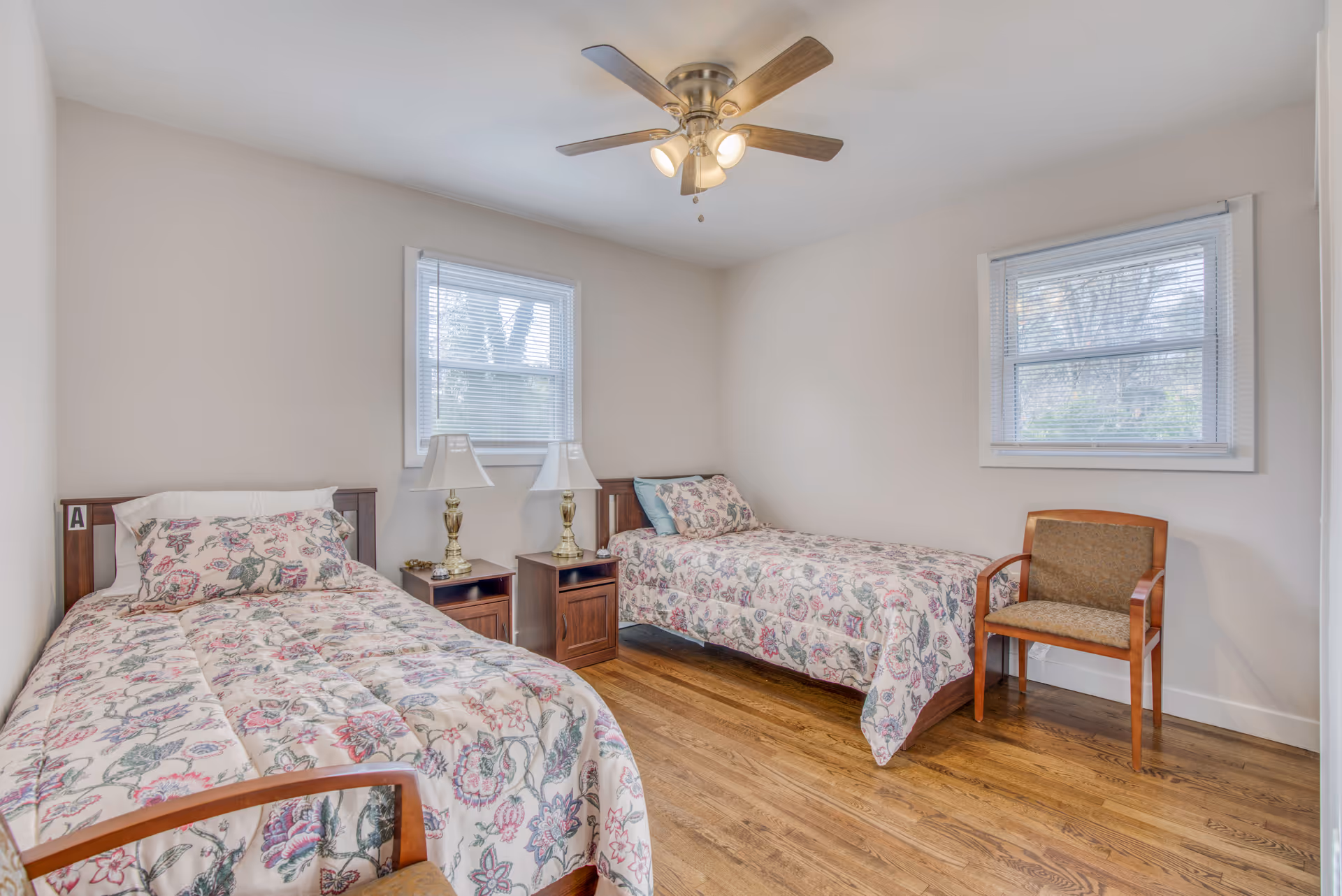 Two twin beds with floral bedding, nightstands, lamps, and a ceiling fan in a bedroom.
