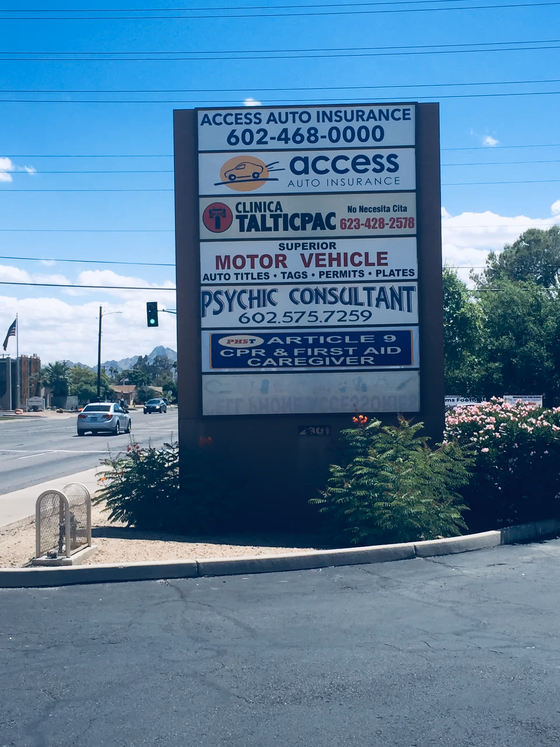 Tall outdoor signboard displaying multiple business ads beside a street and parking.