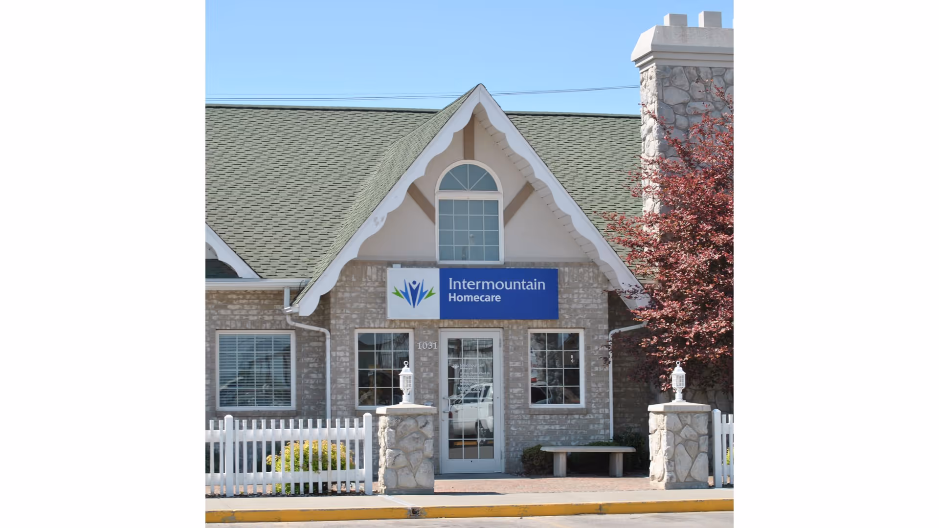 Front view of Intermountain Homecare facility with brick facade, sign, and white fence.