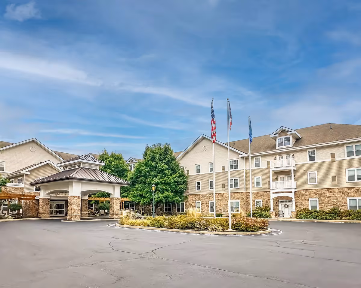 A multi-story Pinebrook of Milford by StoryPoint Group facility exterior with flagpoles and entrance canopy.