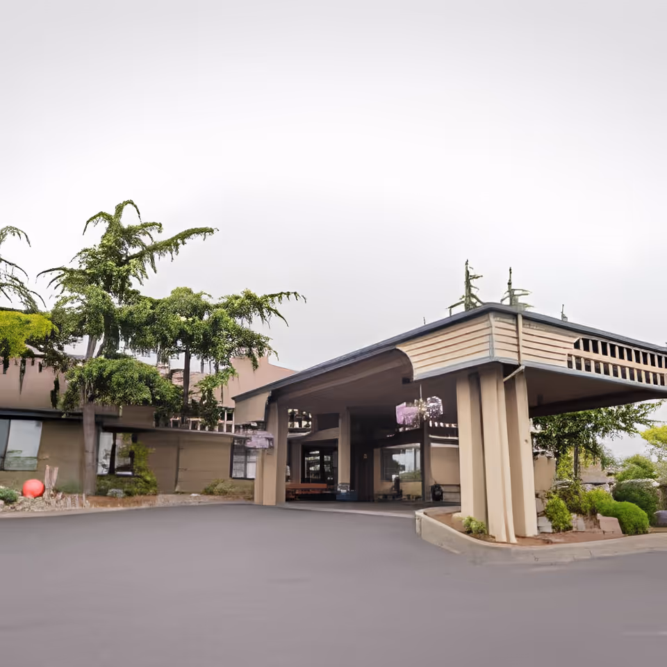 Covered entrance canopy and driveway of a senior living building with trees and landscaping.