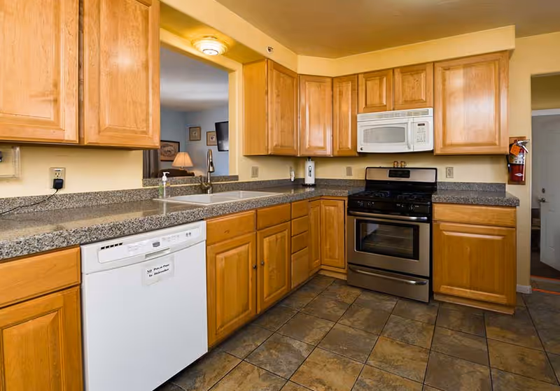 Wooden cabinets line a granite kitchen with sink, dishwasher, and stove.