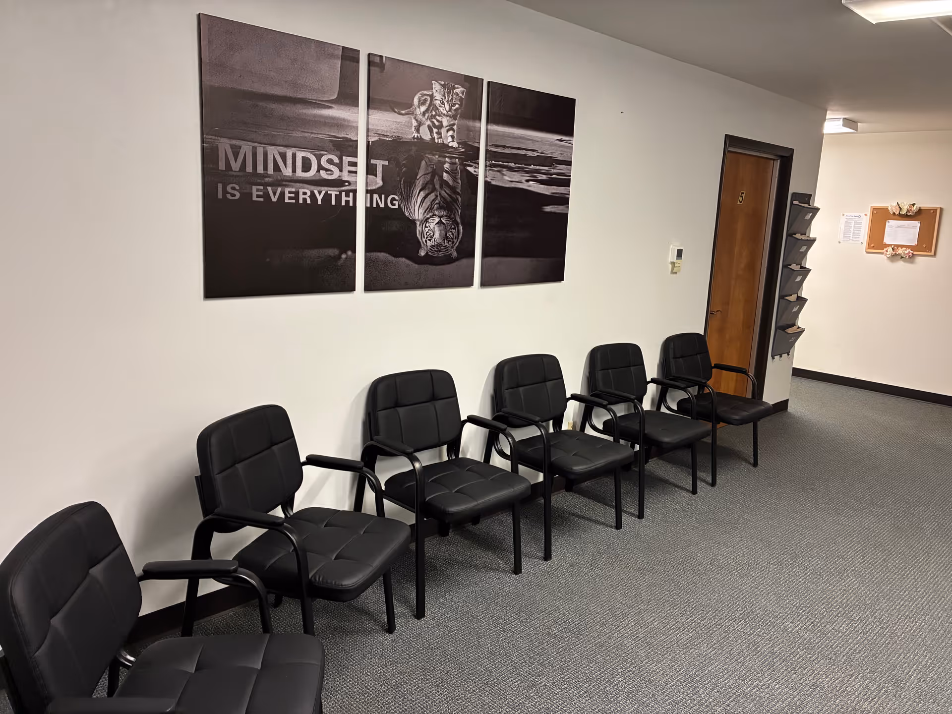 Row of black chairs along a wall with a three-panel tiger mural 'Mindset is Everything'.