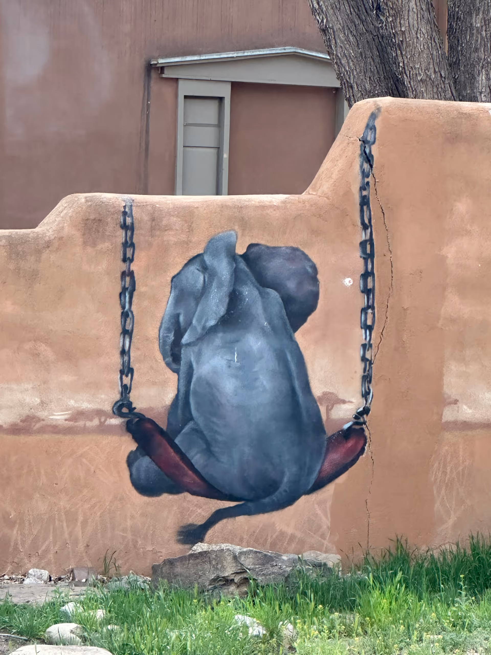 Exterior wall with a gray elephant mural on a tan stucco surface.