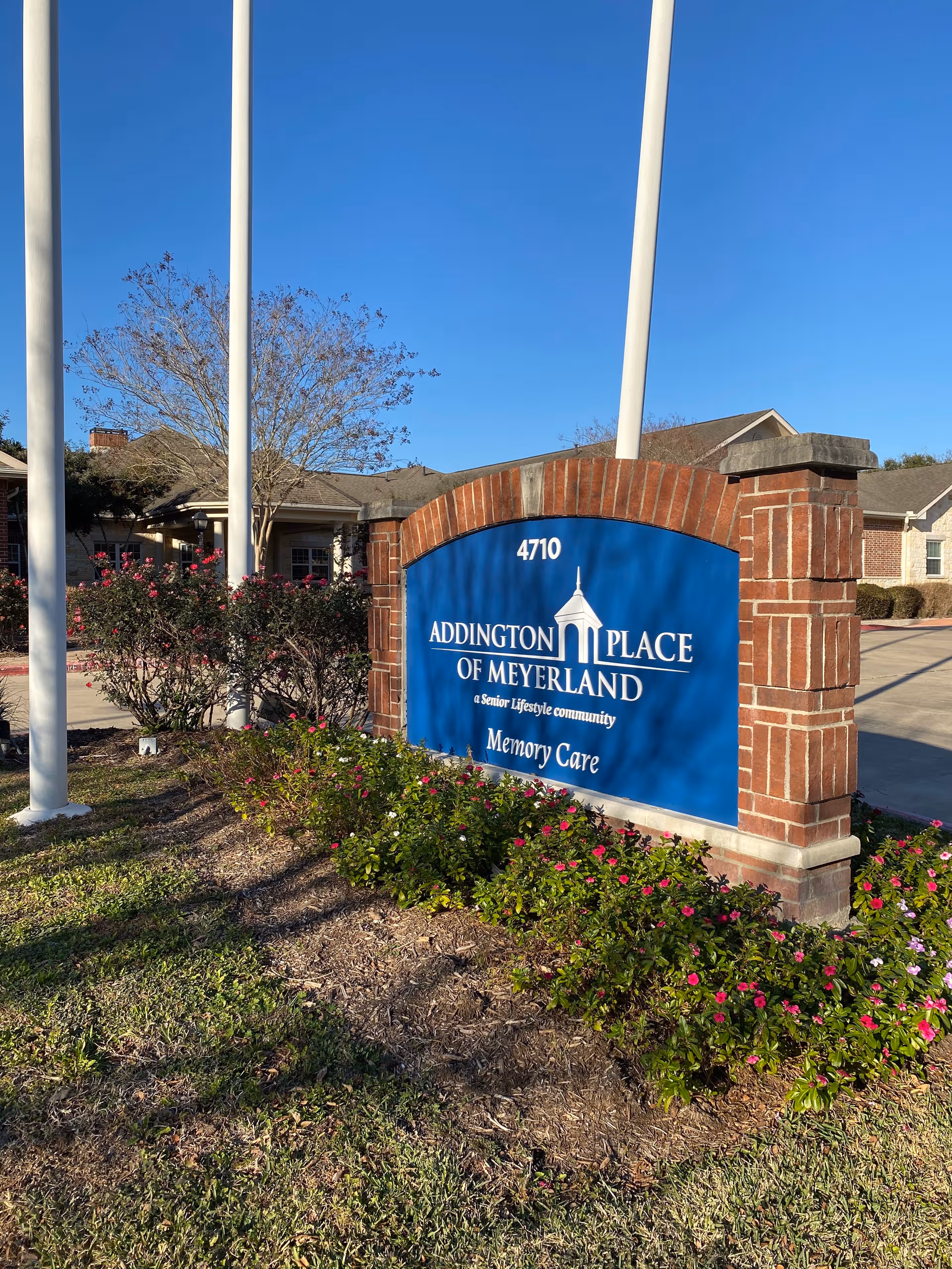 Blue sign reads Addington Place of Meyerland at the entrance, with brick pillars and landscaping.