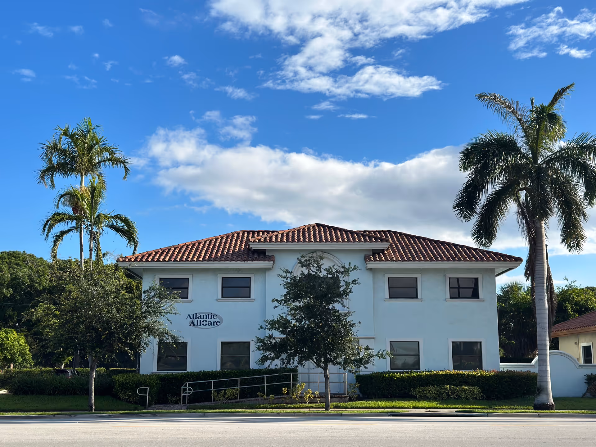 Two-story white building with a red-tiled roof and palm trees against a blue sky.