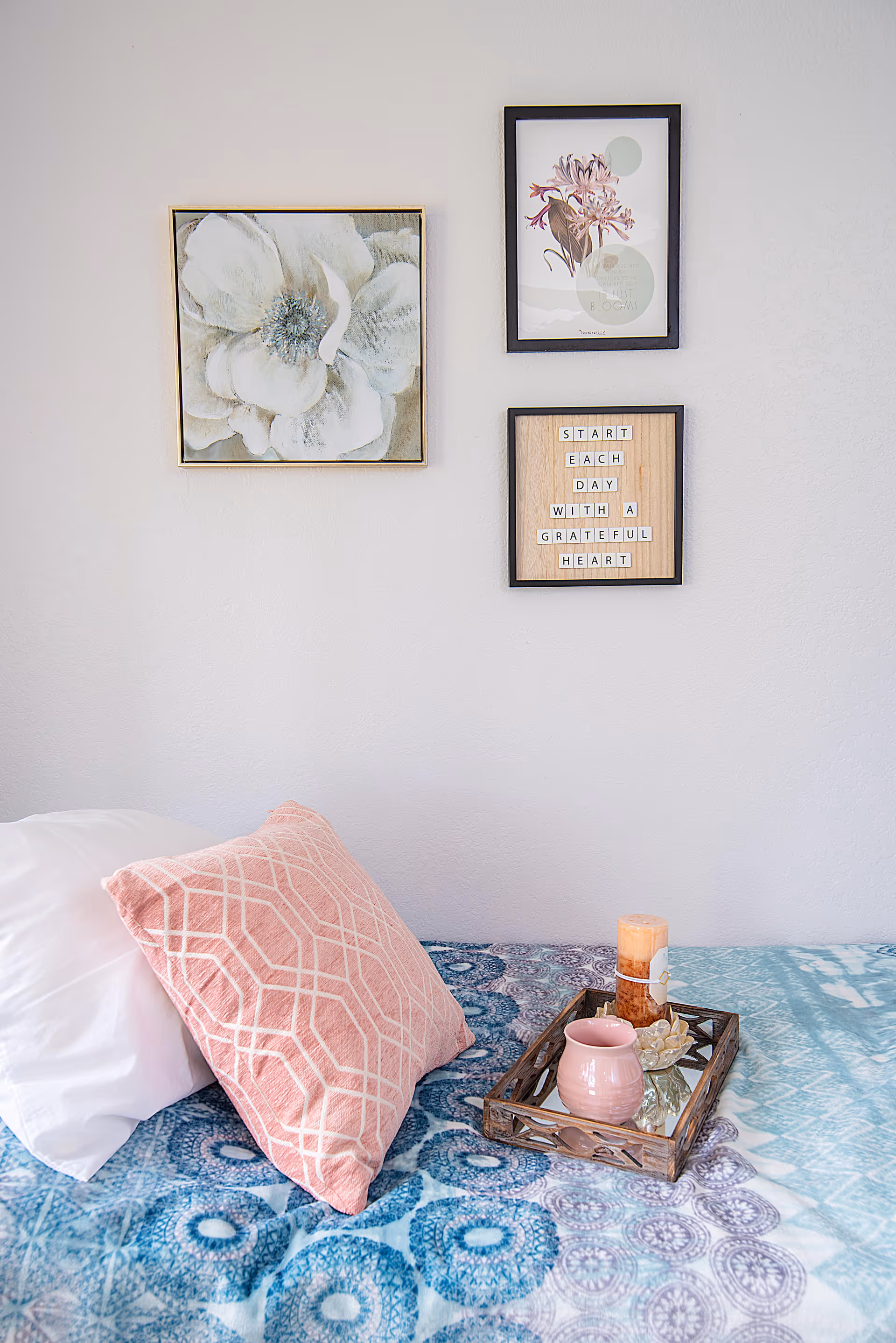 A neatly made bedroom with pink pillow, blue patterned bedspread, and three wall art frames.