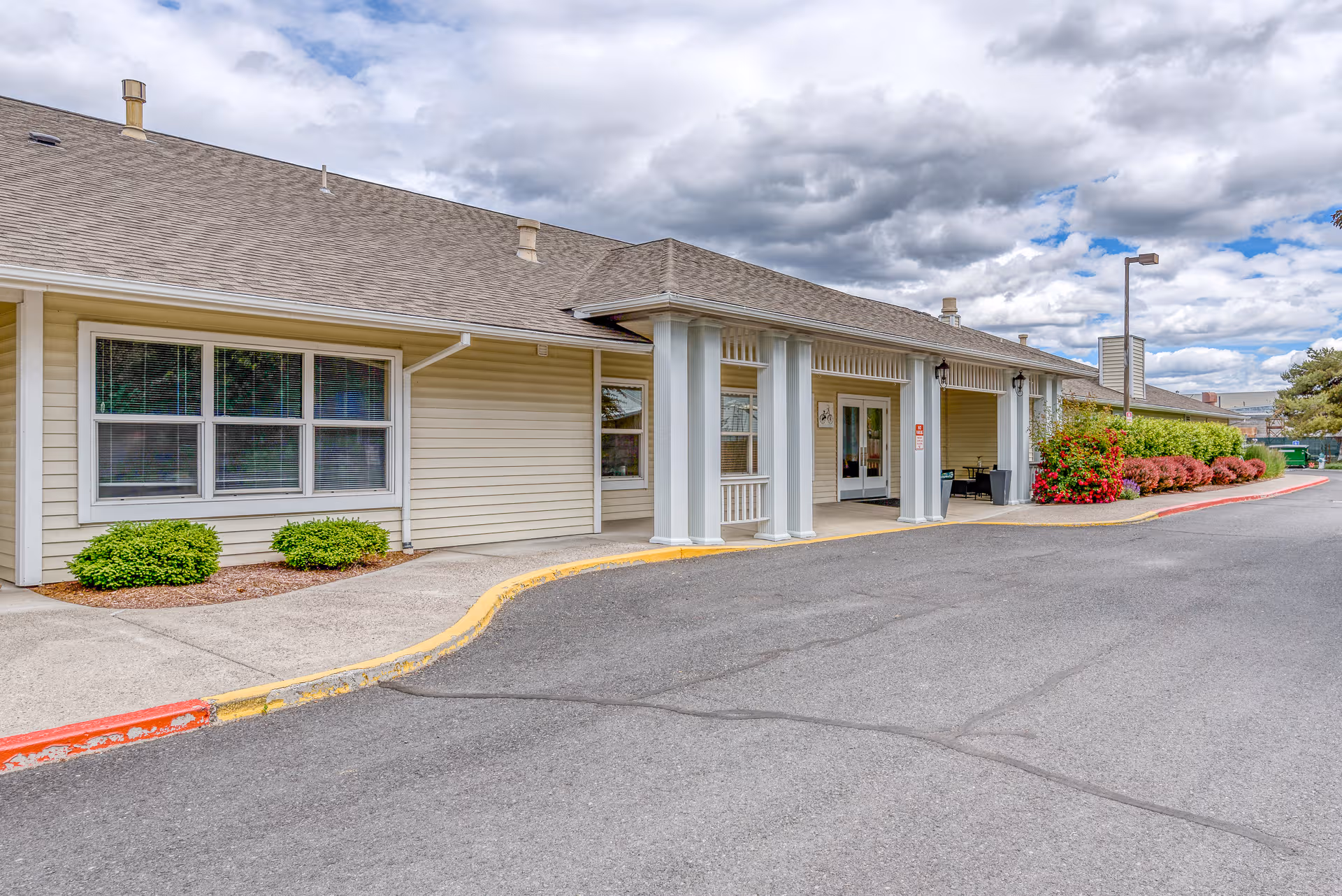 Single-story senior living facility exterior with a covered entrance and landscaped shrubs.