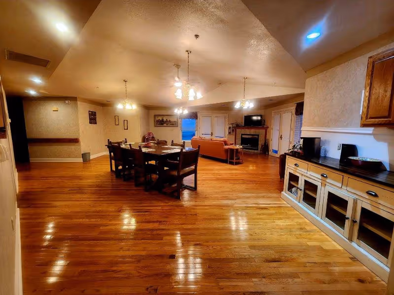 Spacious senior living common area with a dining table, sofa, and wood floors.