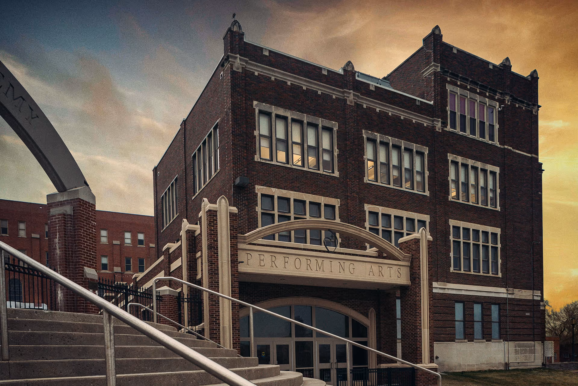 Brick building with arched entrance labeled Performing Arts and front stairs.