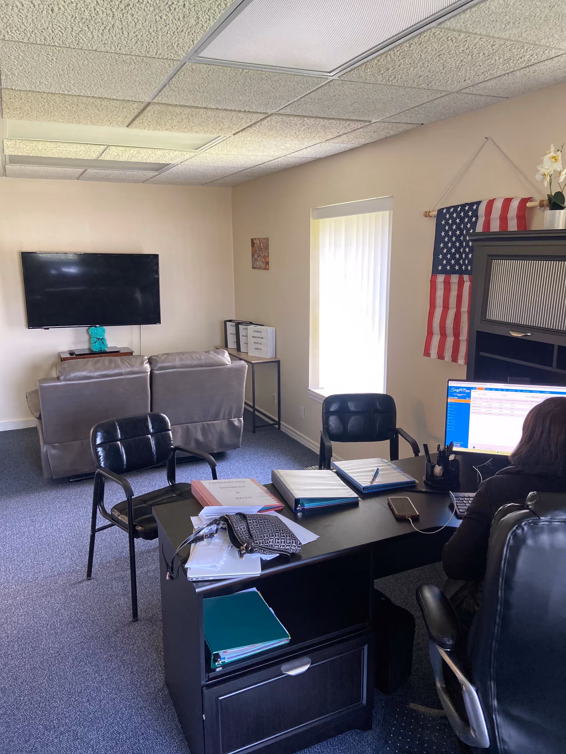 Office-style lounge with desk, computer, couch, wall TV, and American flag.