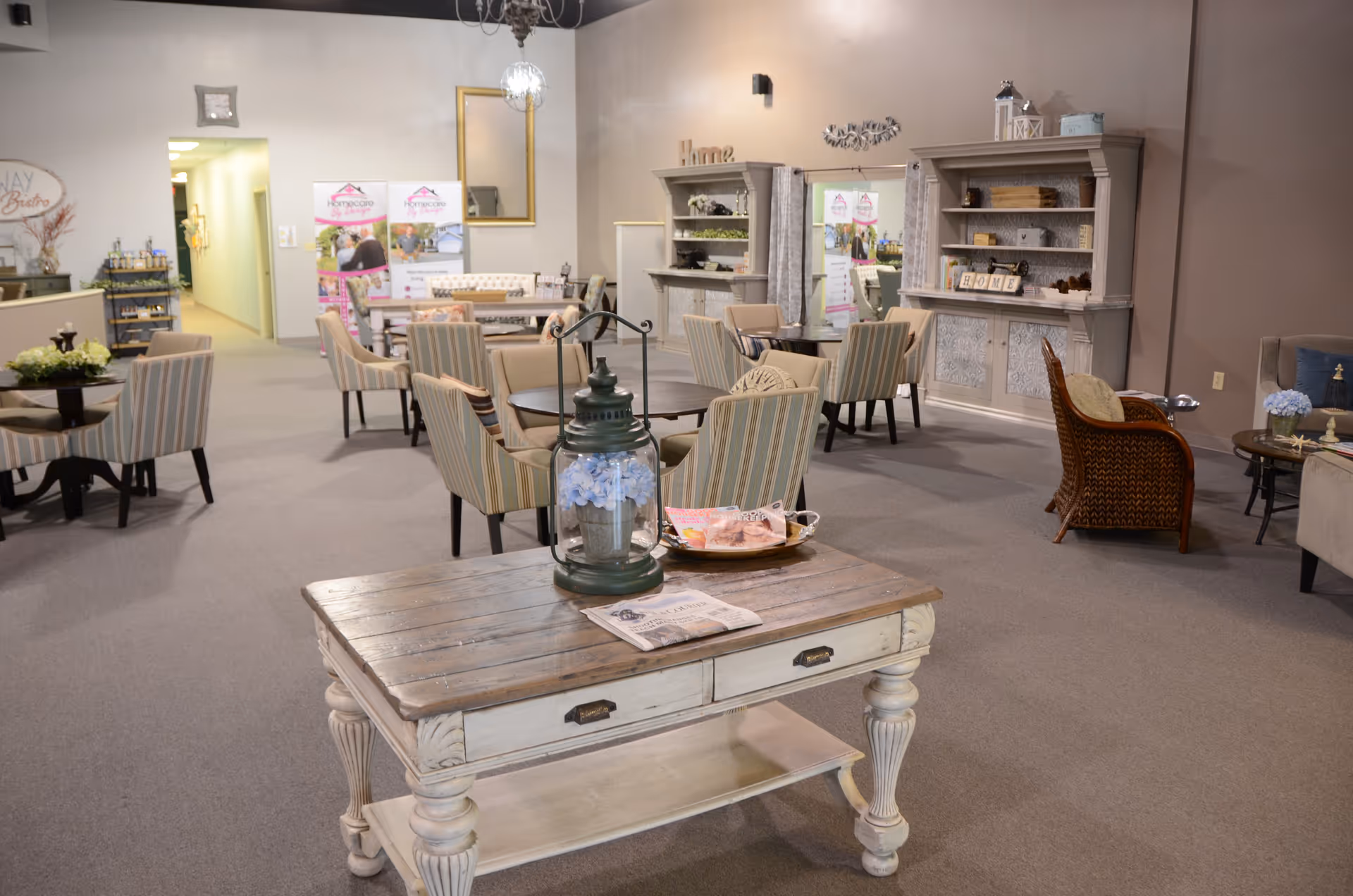 A spacious senior living lounge with striped chairs, coffee tables, and decorative shelving.
