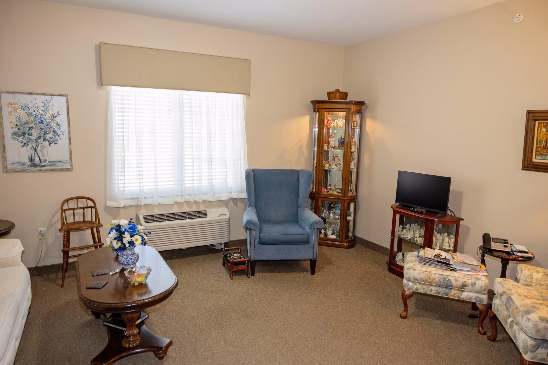 Living room with blue armchair, glass display cabinet, TV, and coffee table.