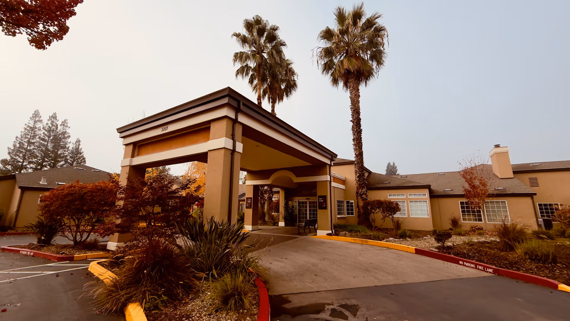 Front view of Eskaton Village Carmichael Care Center entrance with palm trees and driveway.