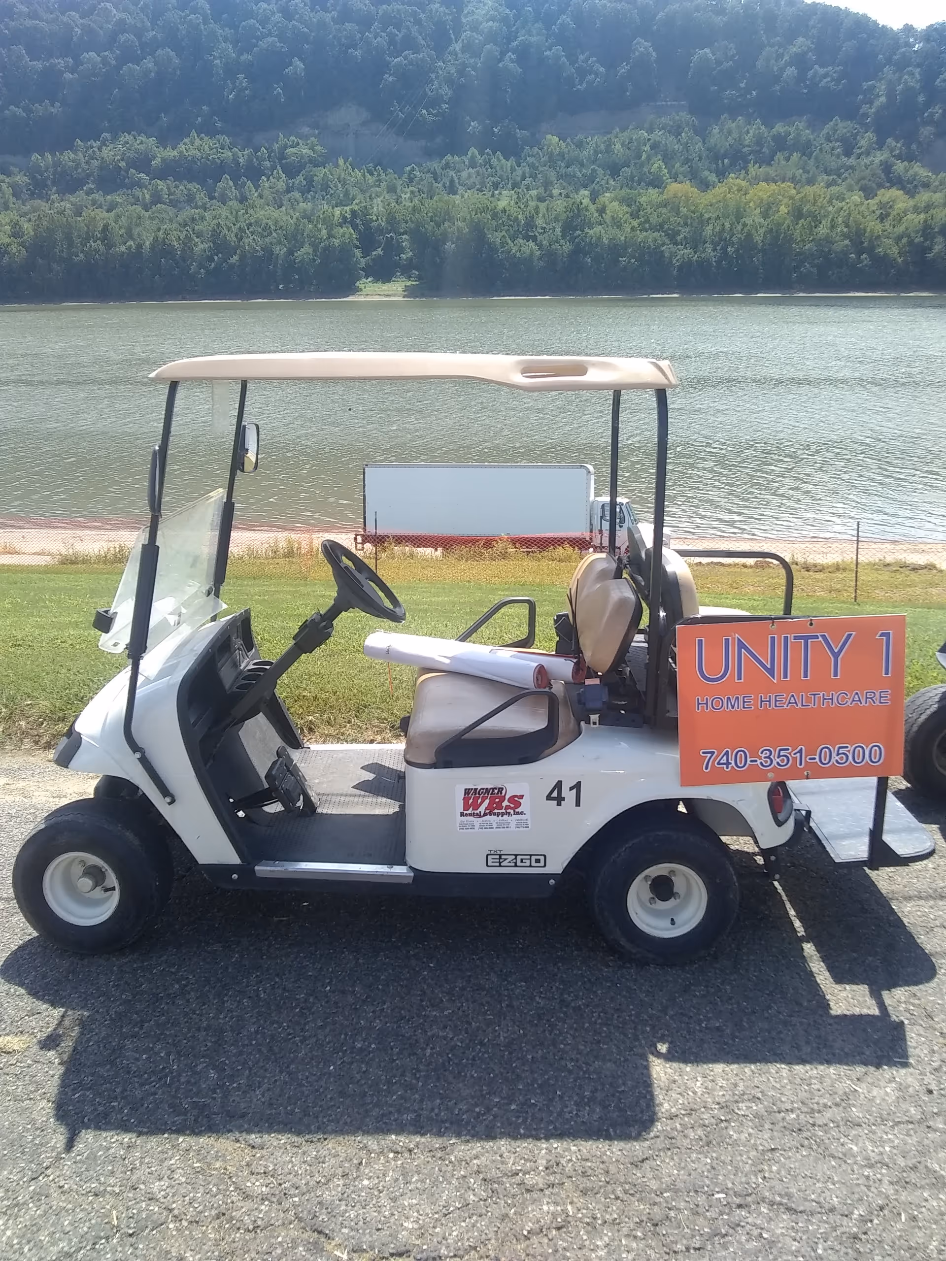 White golf cart with Unity 1 Home Healthcare sign parked near a lake.