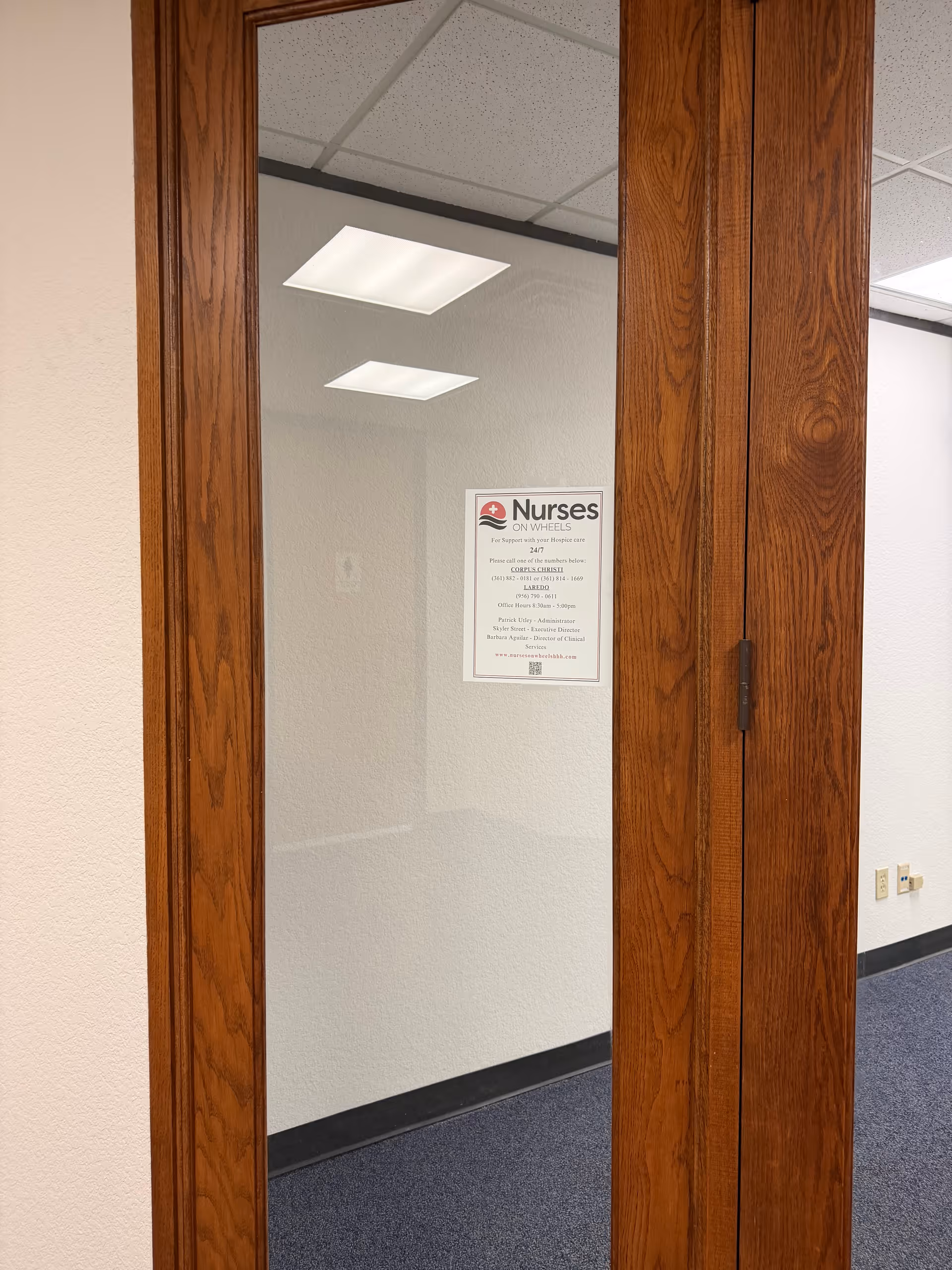 Wood-framed glass doorway opens to a hallway with a Nurses On Wheels sign.