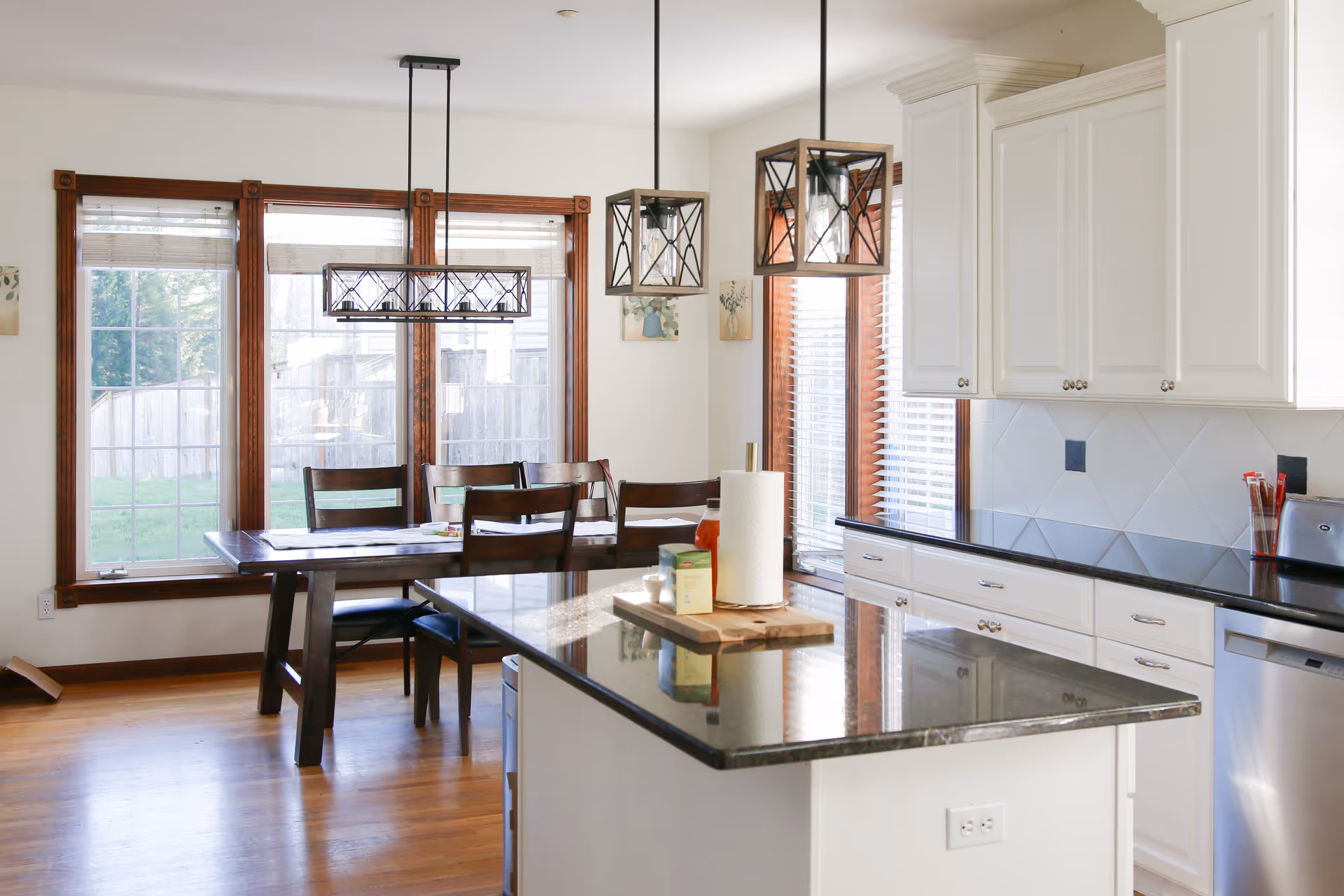 Bright kitchen with island, white cabinets, stainless appliances, and a dining table by large windows.