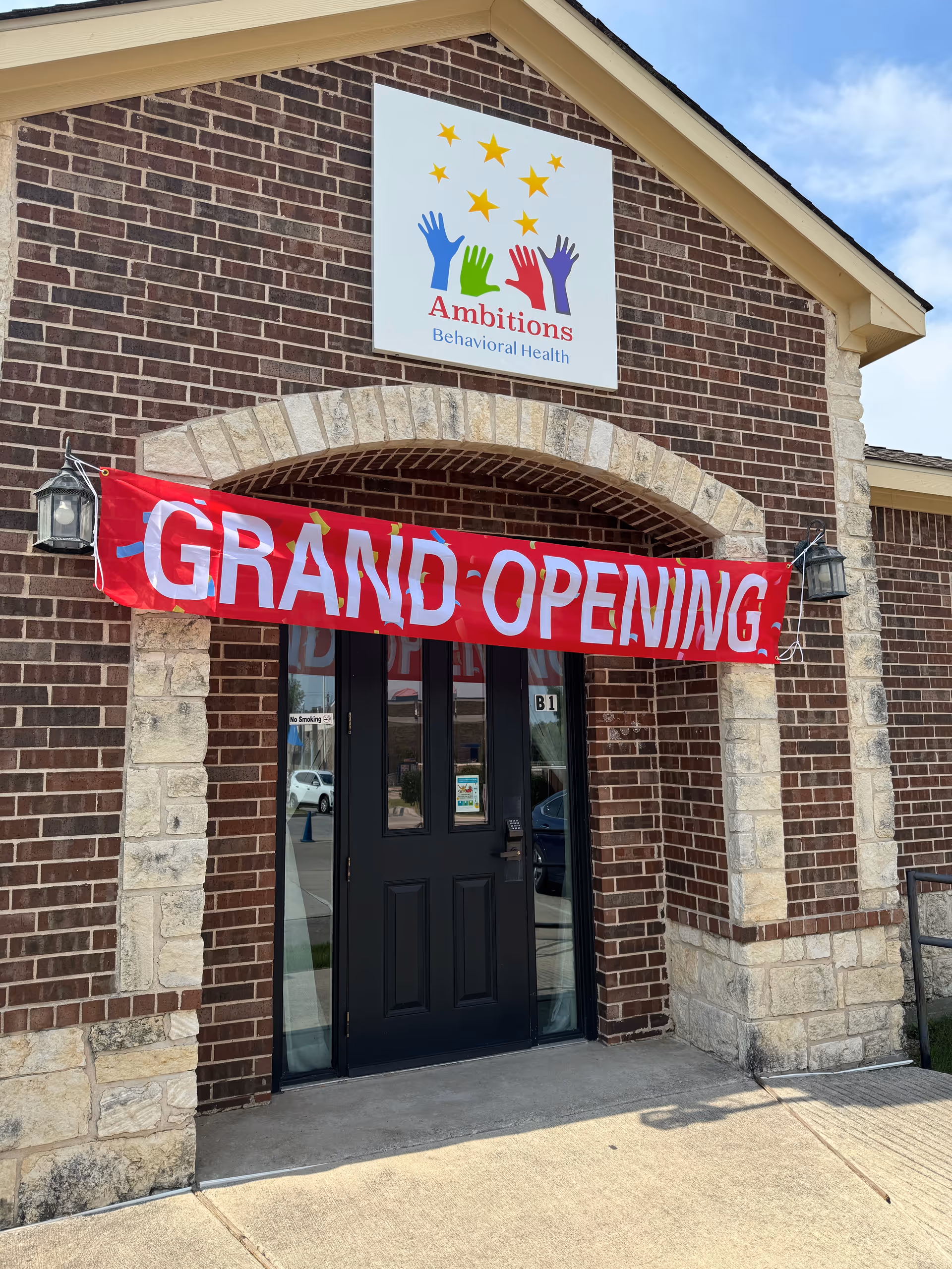 Brick building exterior with a grand-opening banner and Ambitions Behavioral Health sign.