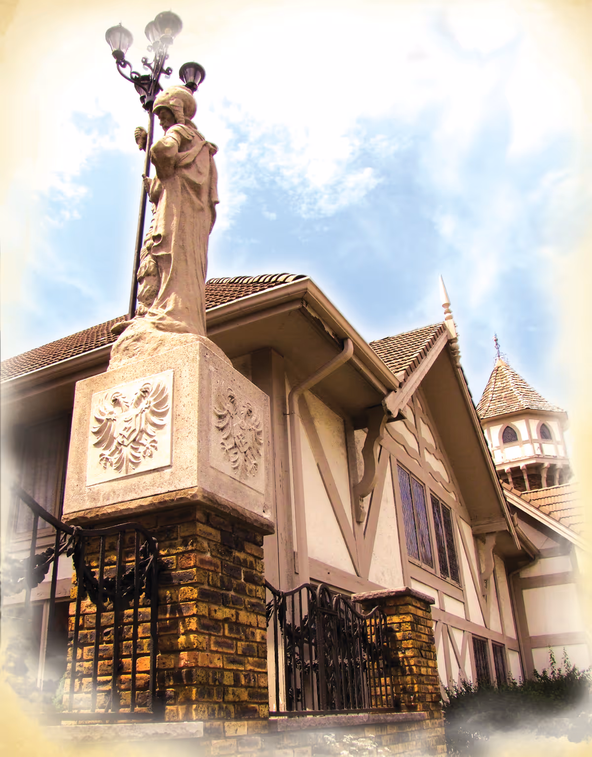 Exterior view of a grand, ornate building with brick pillars and statue beneath a blue sky.