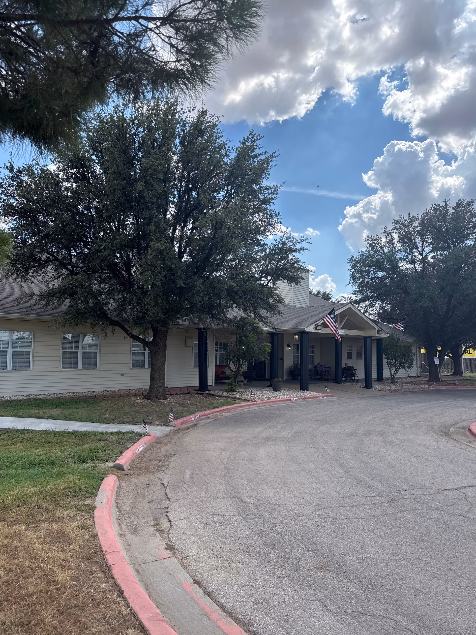 Front exterior of a senior living facility with a curved driveway and trees.