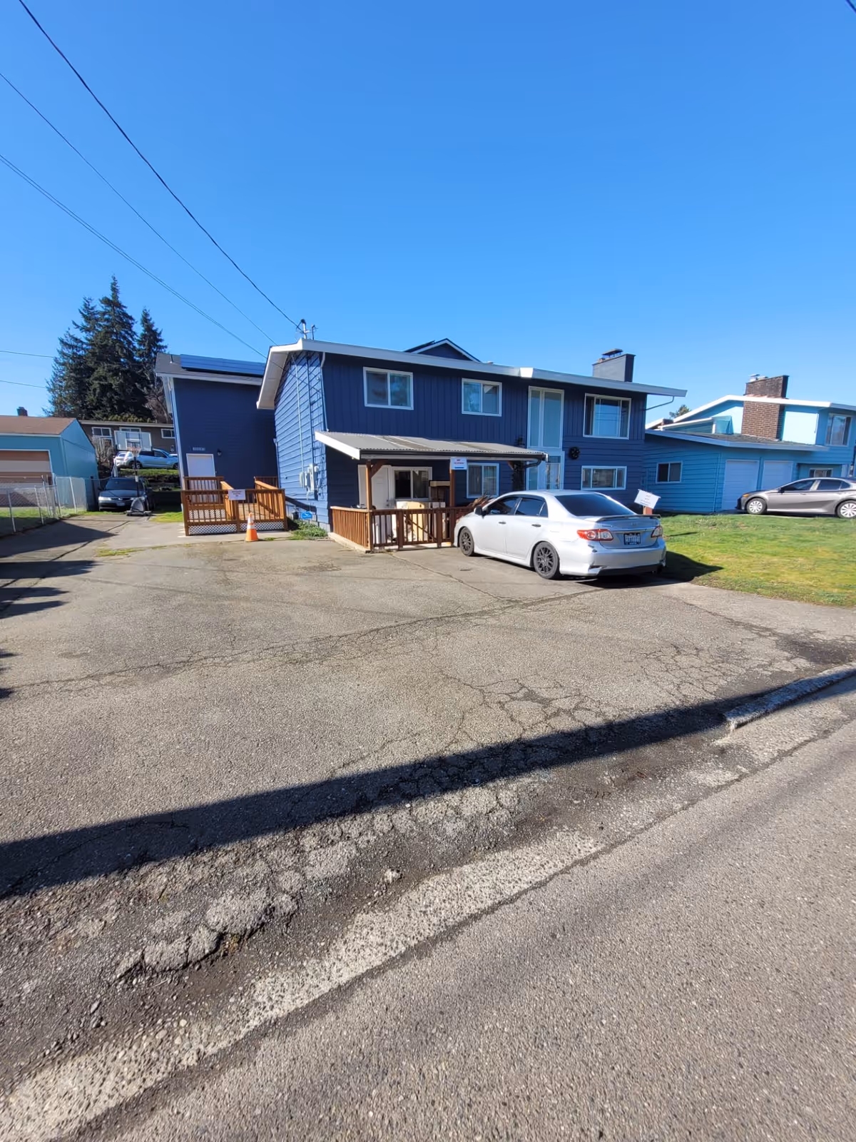 Blue two-story house with a small covered porch and a white car parked in the driveway under a clear blue sky.