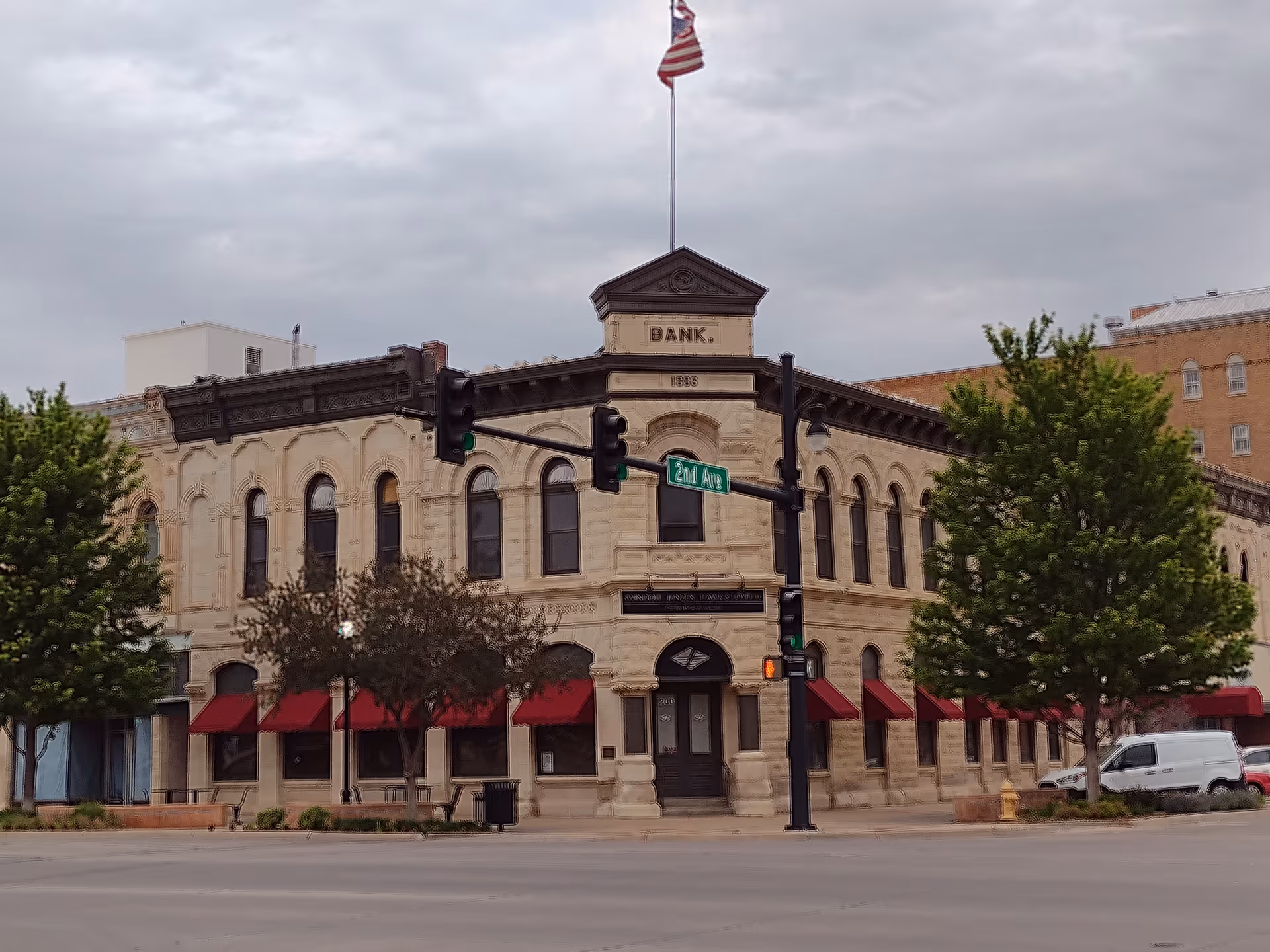 Historic bank building with arched windows and red awnings along a city street.