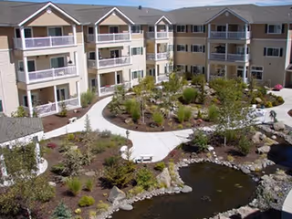 Courtyard of a multi-story retirement building with landscaped paths, a pond, and balconies.