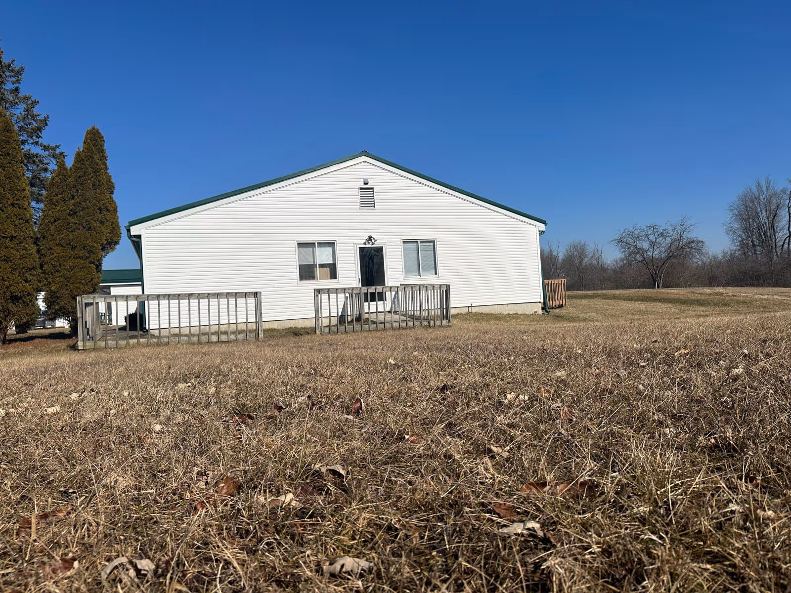 White single-story building with green trim stands in a wide, leaf-strewn field.