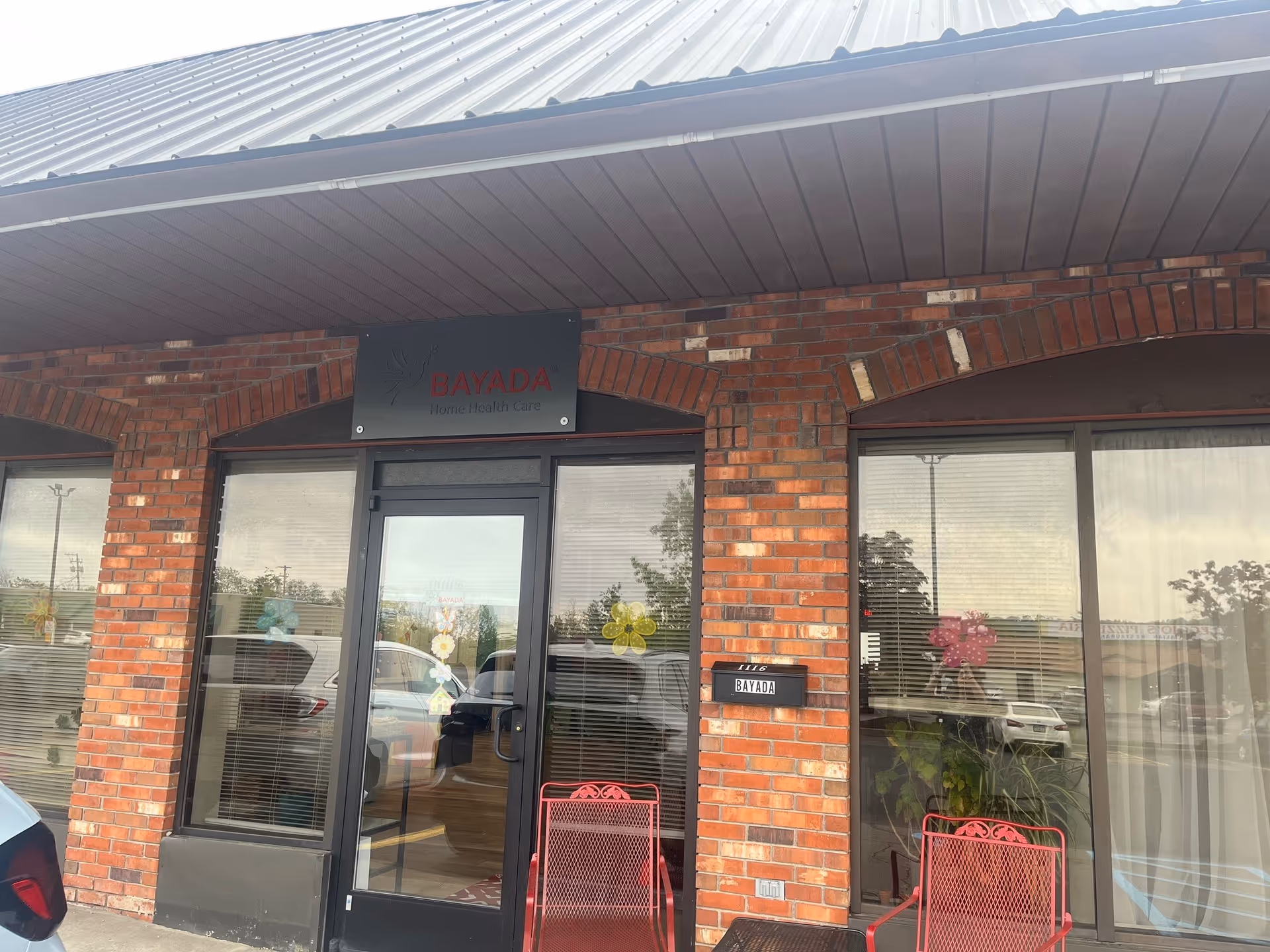 Brick building entrance with BAYADA sign, glass doors, and red chairs outside