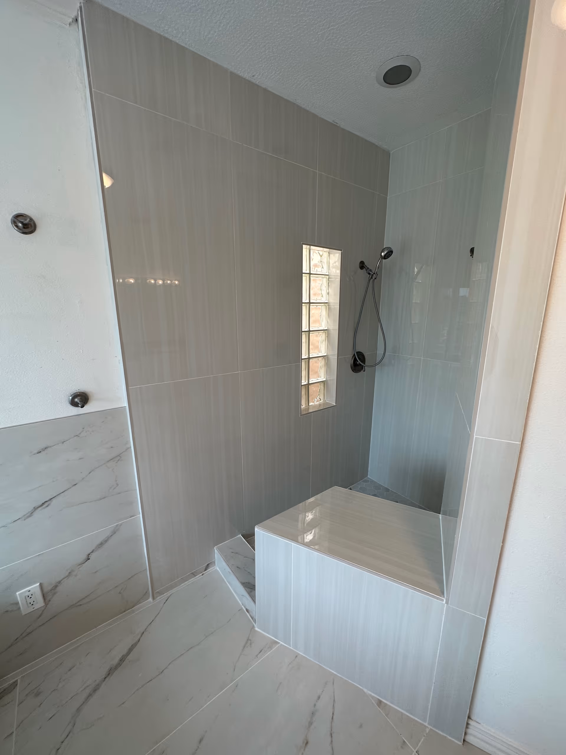 Modern tiled bathroom shower with built-in bench and handheld shower.