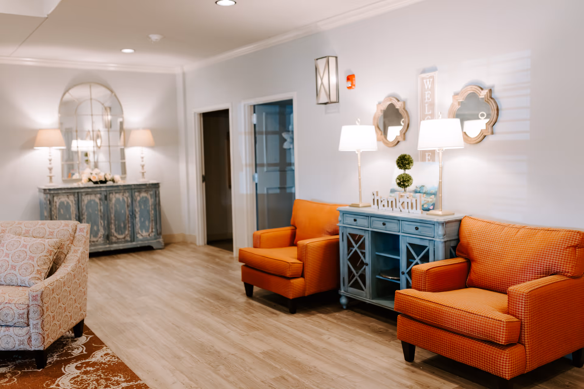 Cozy living room lobby with orange armchairs, blue console, and decorative lamps.