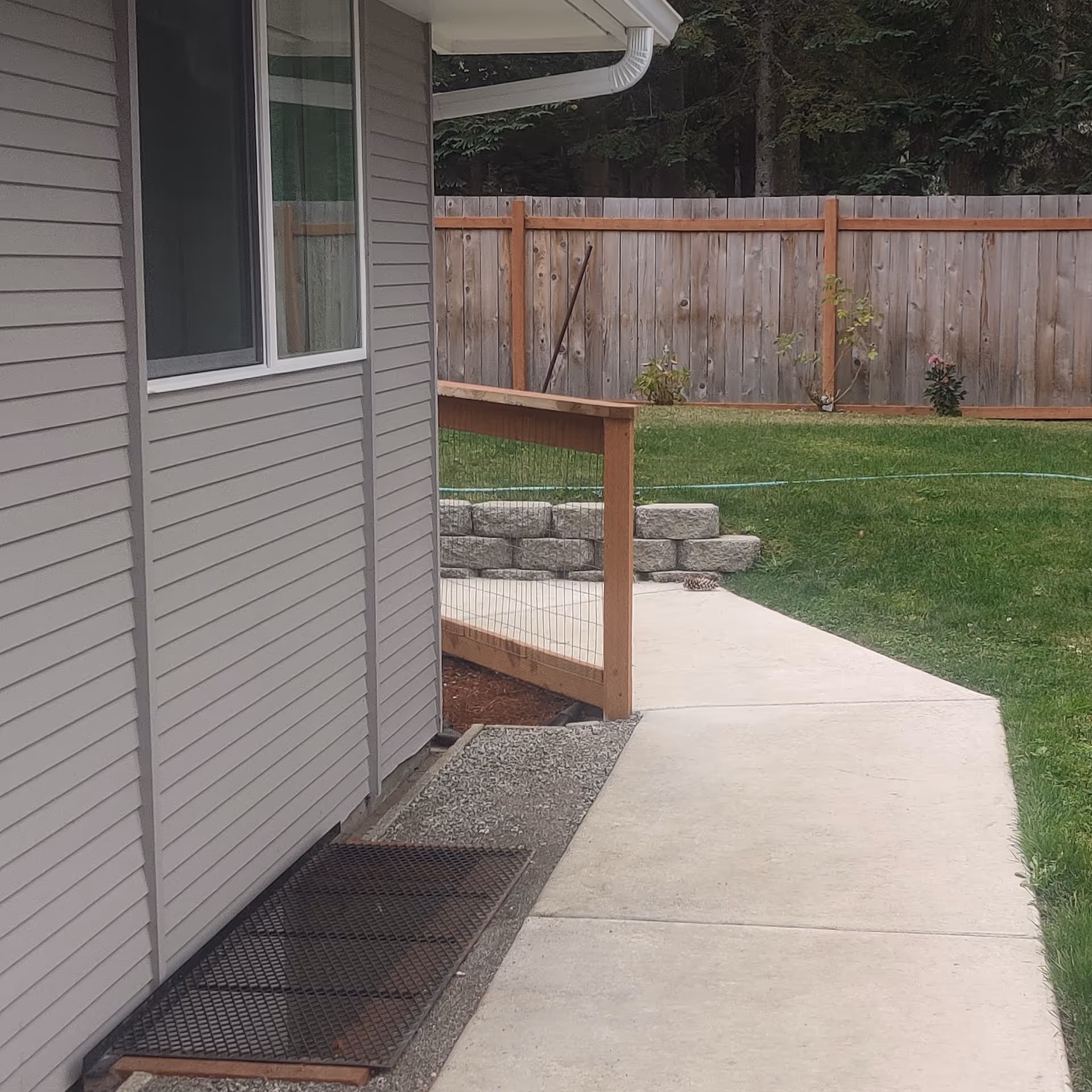 Exterior view of a residential building with beige siding, window, ramp, and wooden fence.