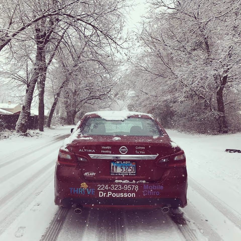 Red promotional car advertising 365 Chiropractic sits on a snowy street.