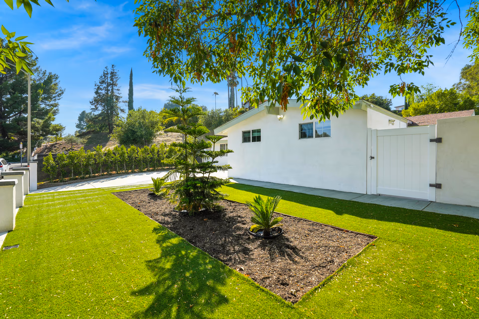 Bright white single-story building with manicured lawn, small garden bed, and a white gate.