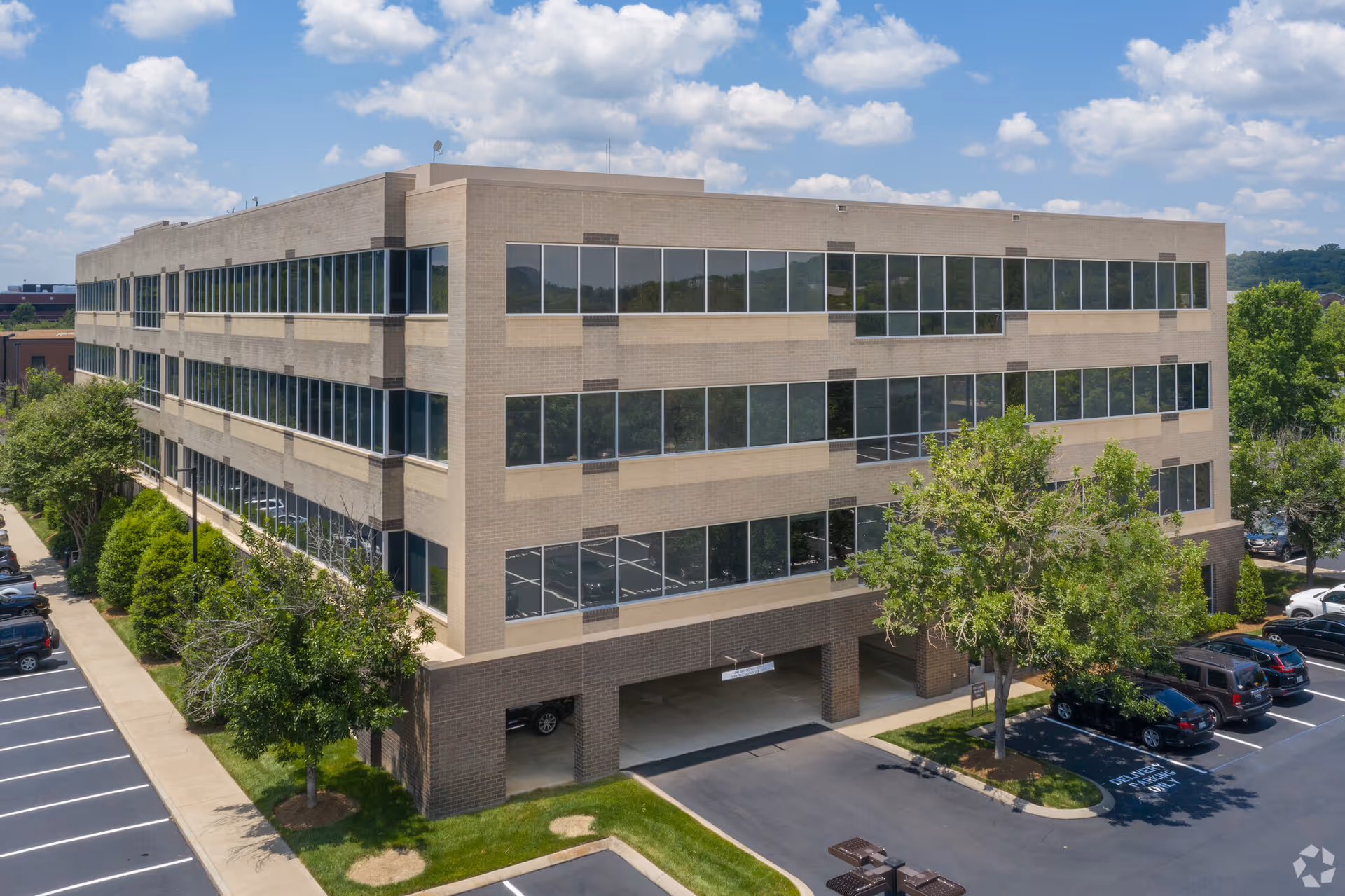 A modern, four-story building with expansive glass windows and a parking lot.