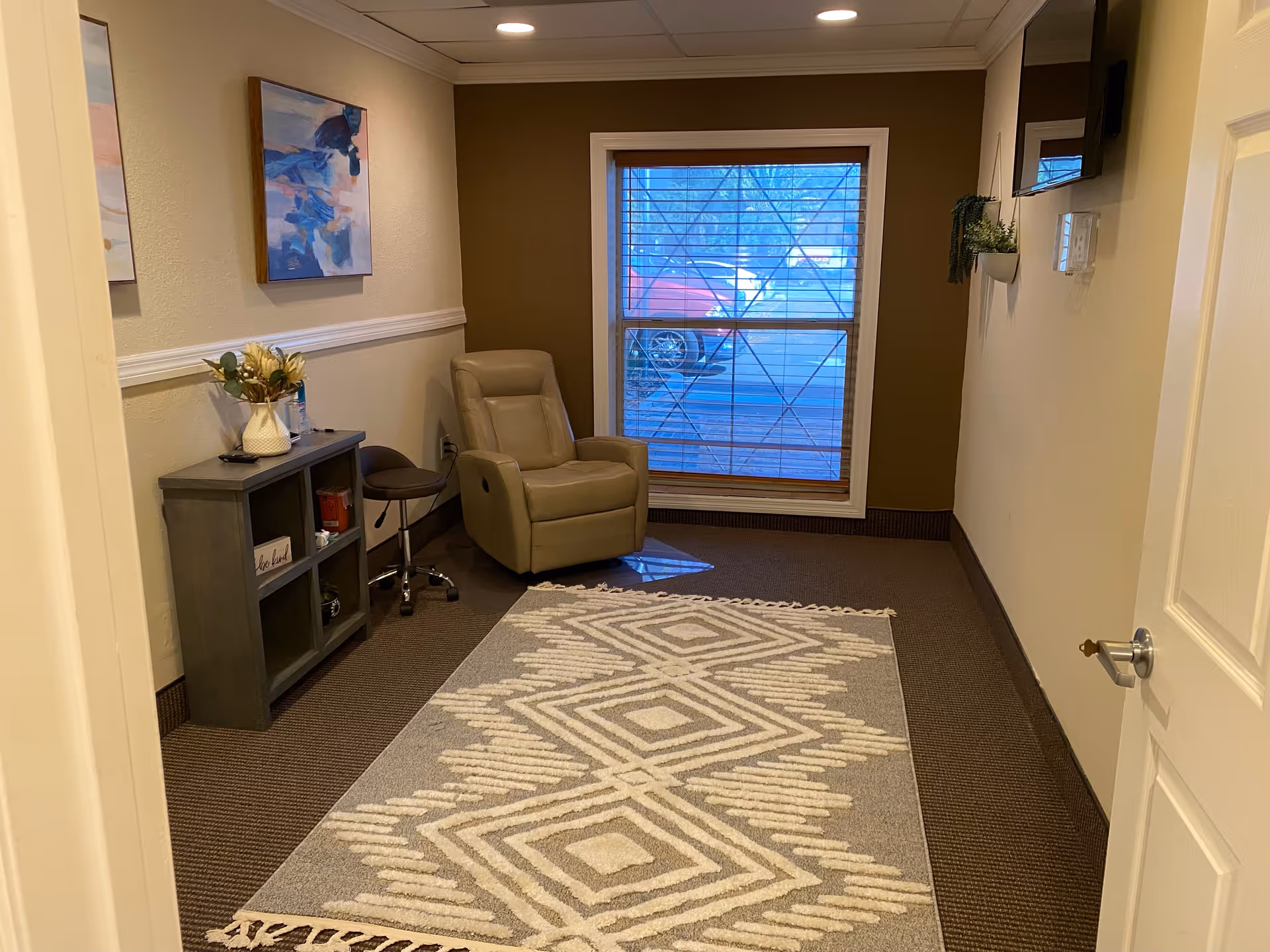 Cozy interior lounge with beige armchair, rug, and window blinds.
