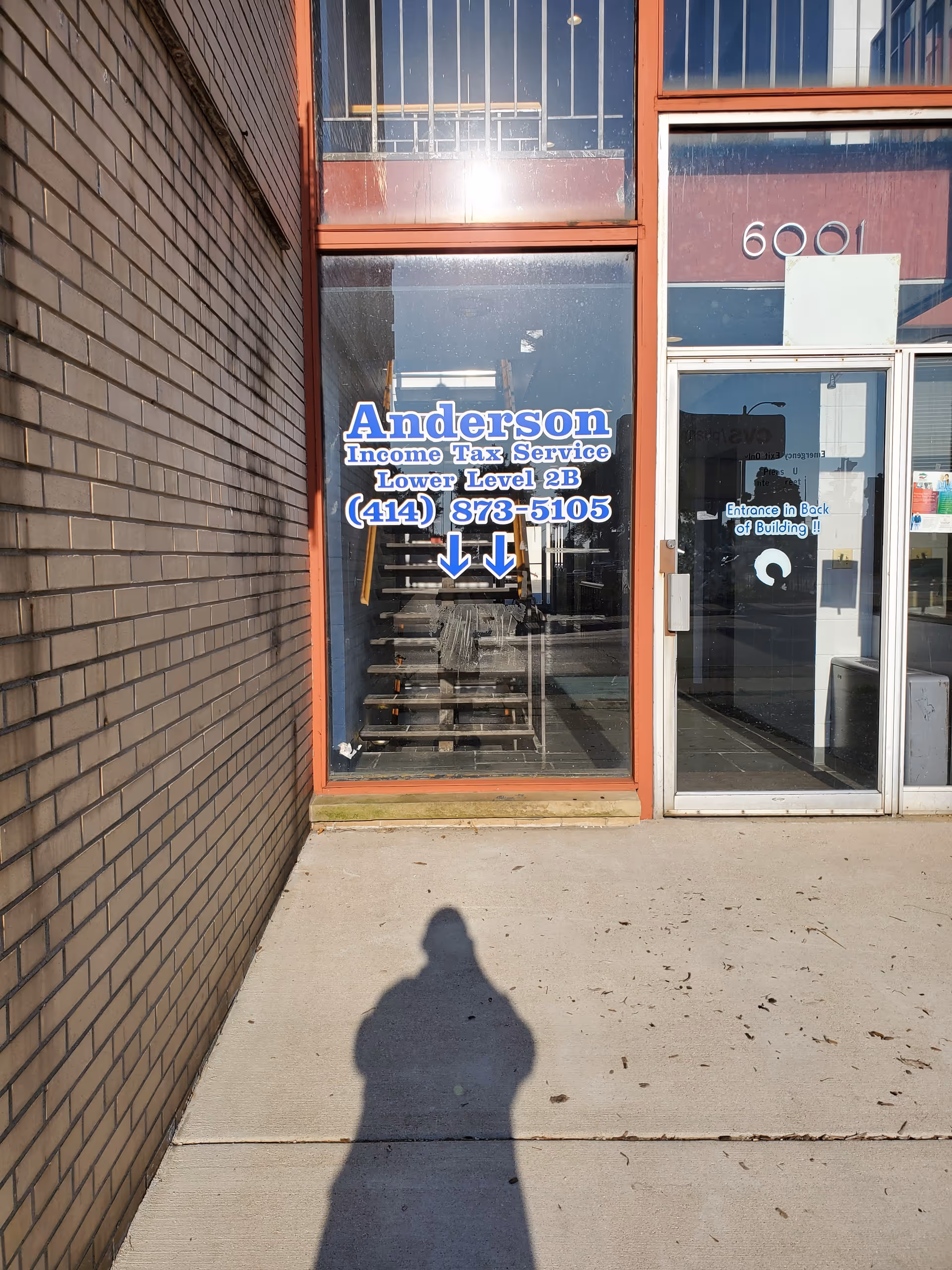 Glass storefront with Anderson Income Tax Service sign, stairs visible inside, sidewalk shadow foreground.