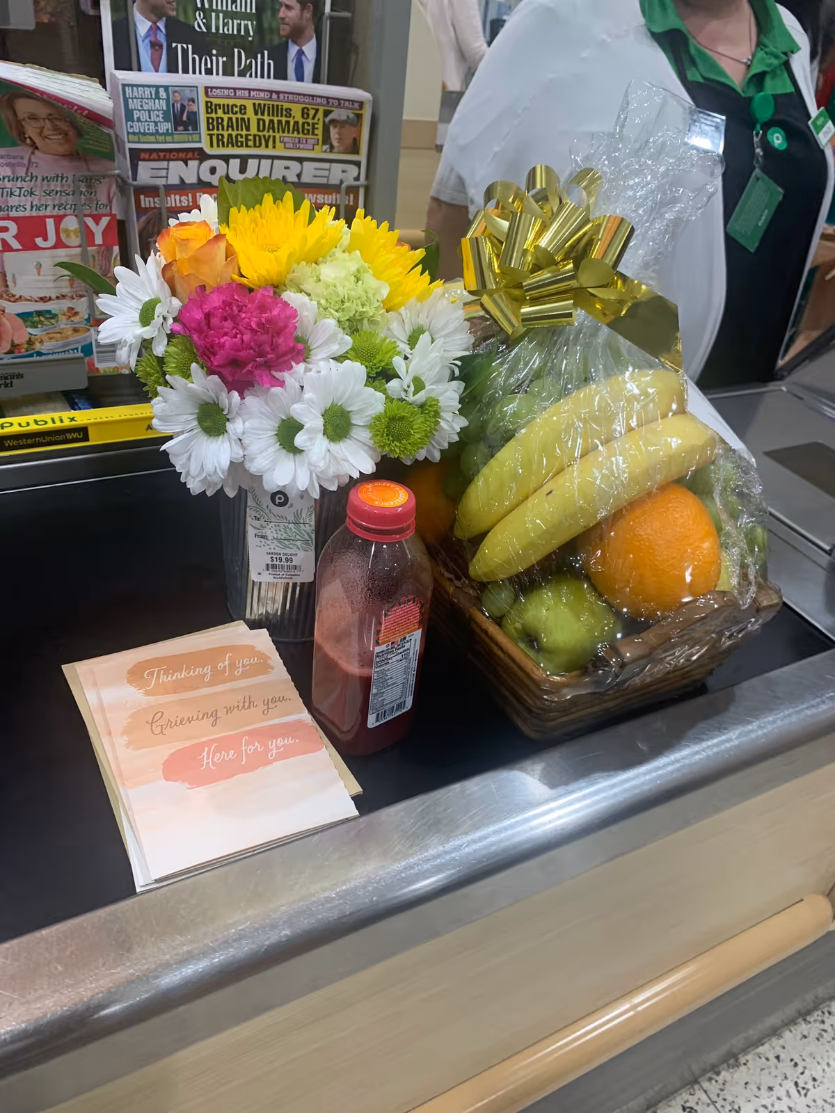 A colorful bouquet and fruit basket sit on a reception counter beside magazines.
