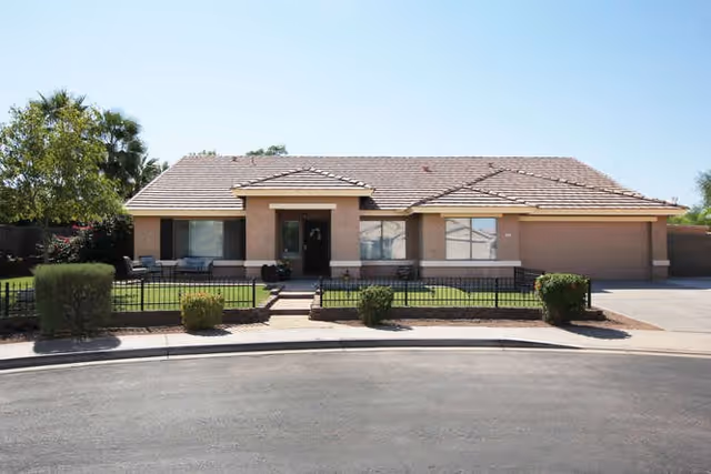 Single-story suburban stucco building with a tiled roof, front lawn, low fence and a driveway leading to a two-car garage.
