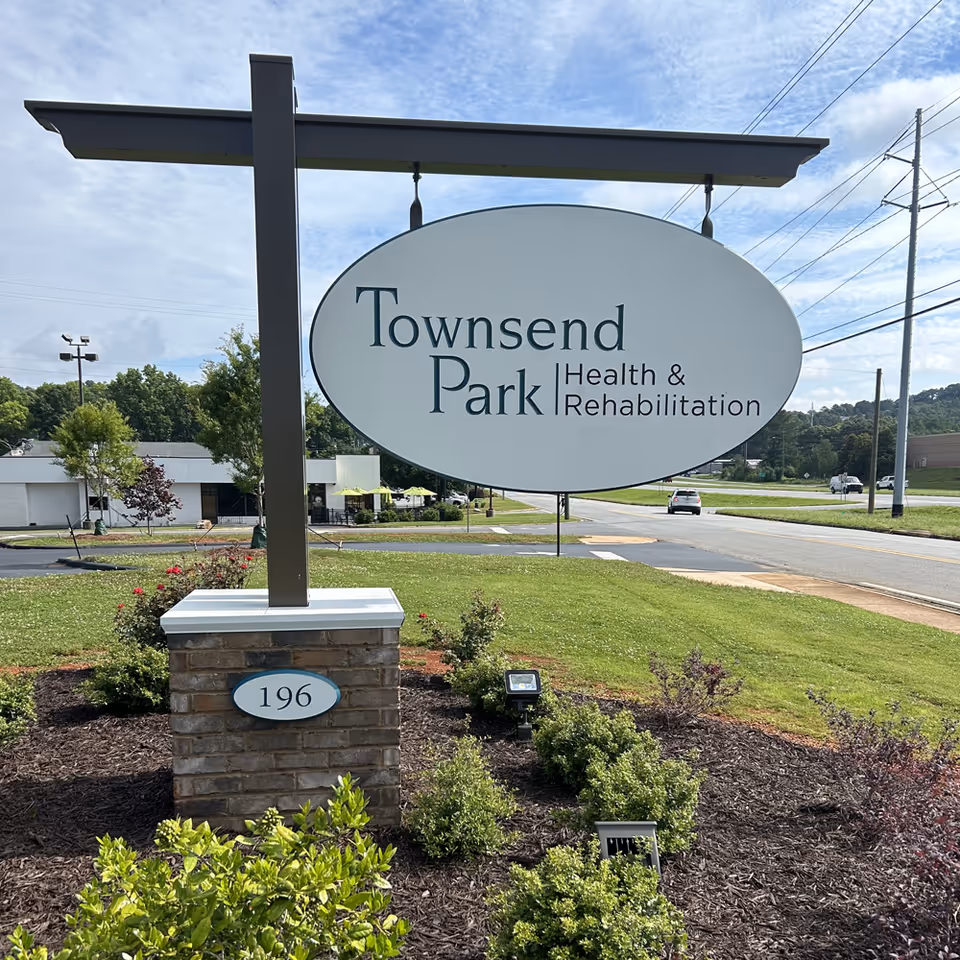 A large roadside sign reading "Townsend Park Health & Rehabilitation" mounted on a post in landscaped grounds with a building and road visible behind it.