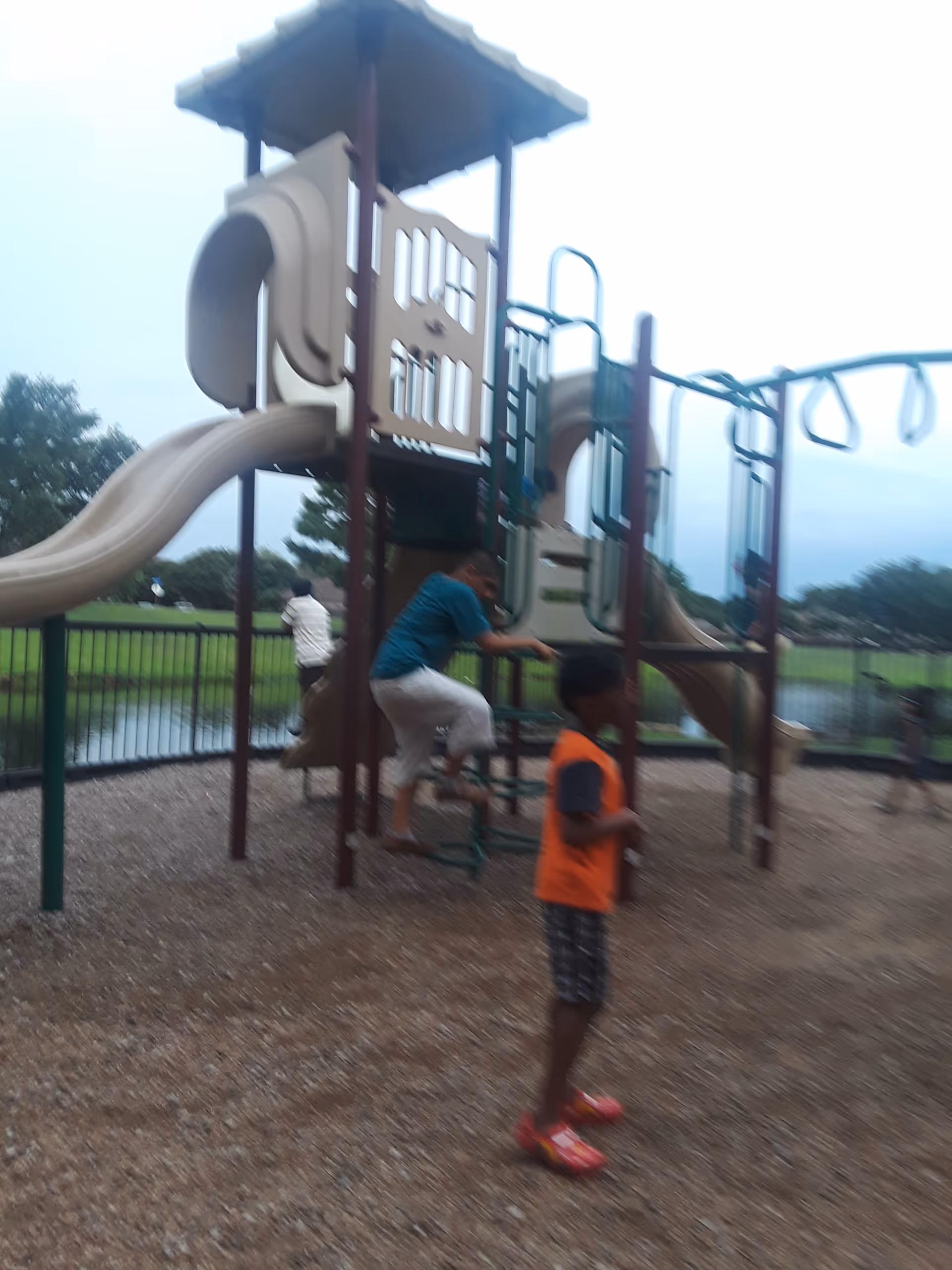 Outdoor playground with a multi-slide structure and people playing nearby.