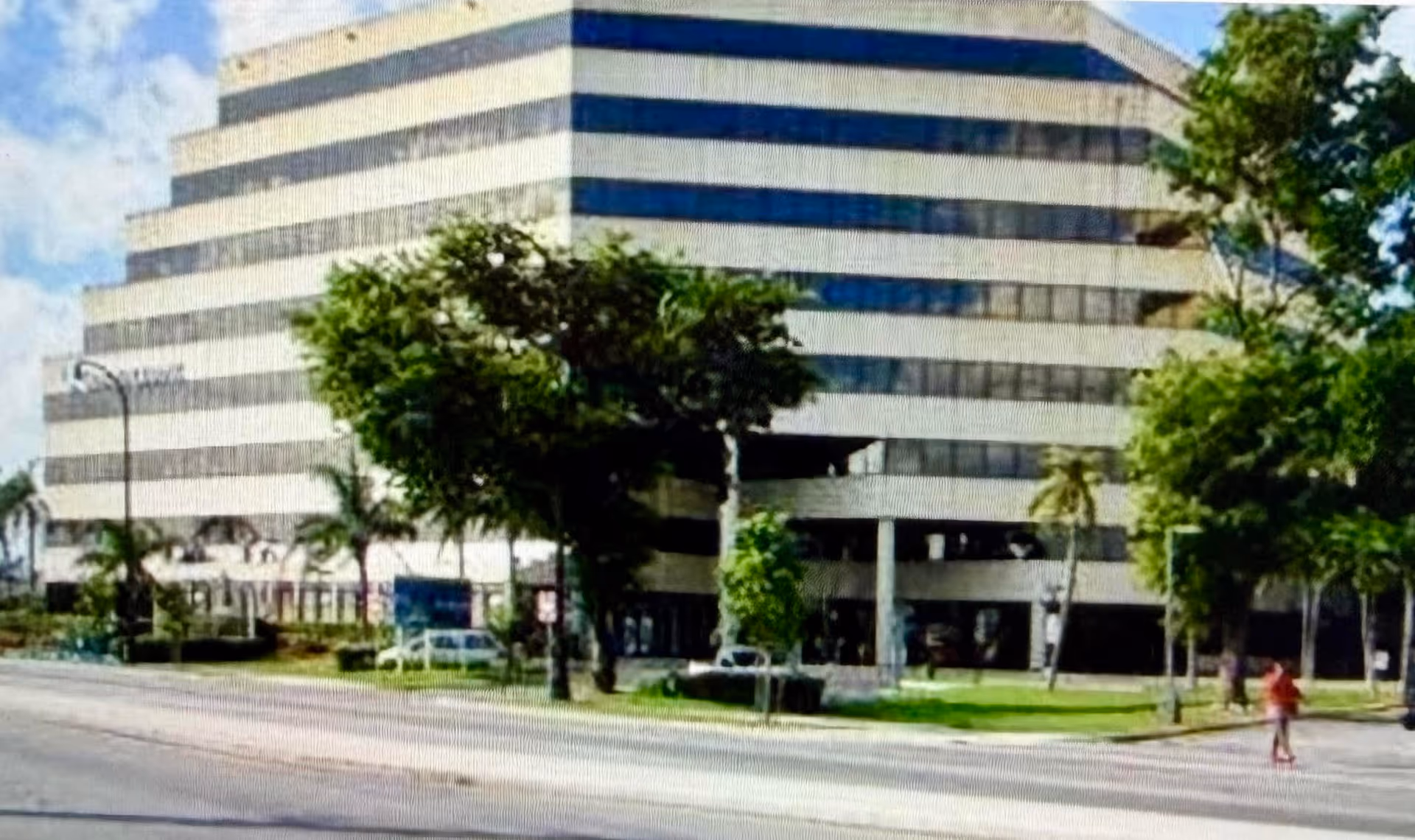 Exterior view of a modern, multi-story building with trees and a street in front.