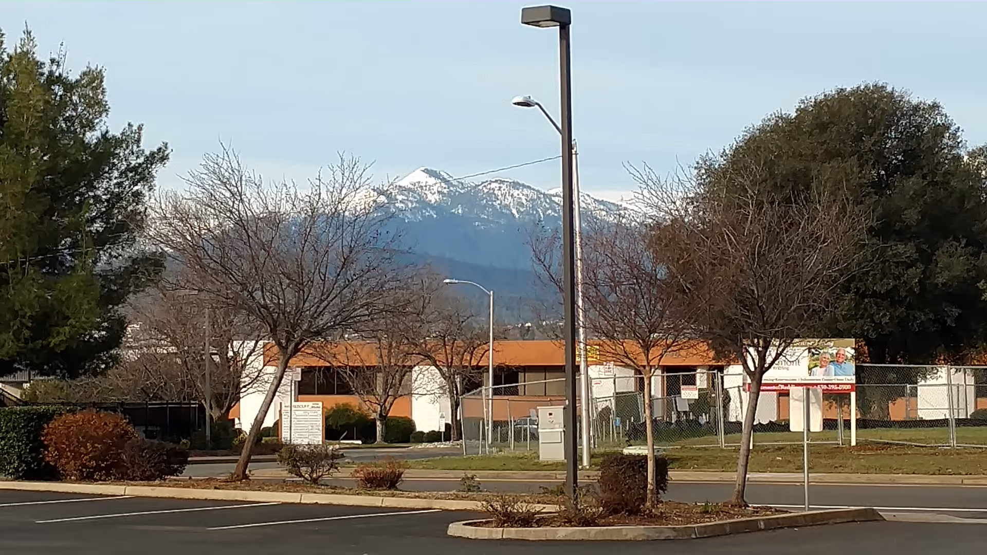 Exterior view of Oakmont of Redding with bare trees, fencing, and distant mountains.