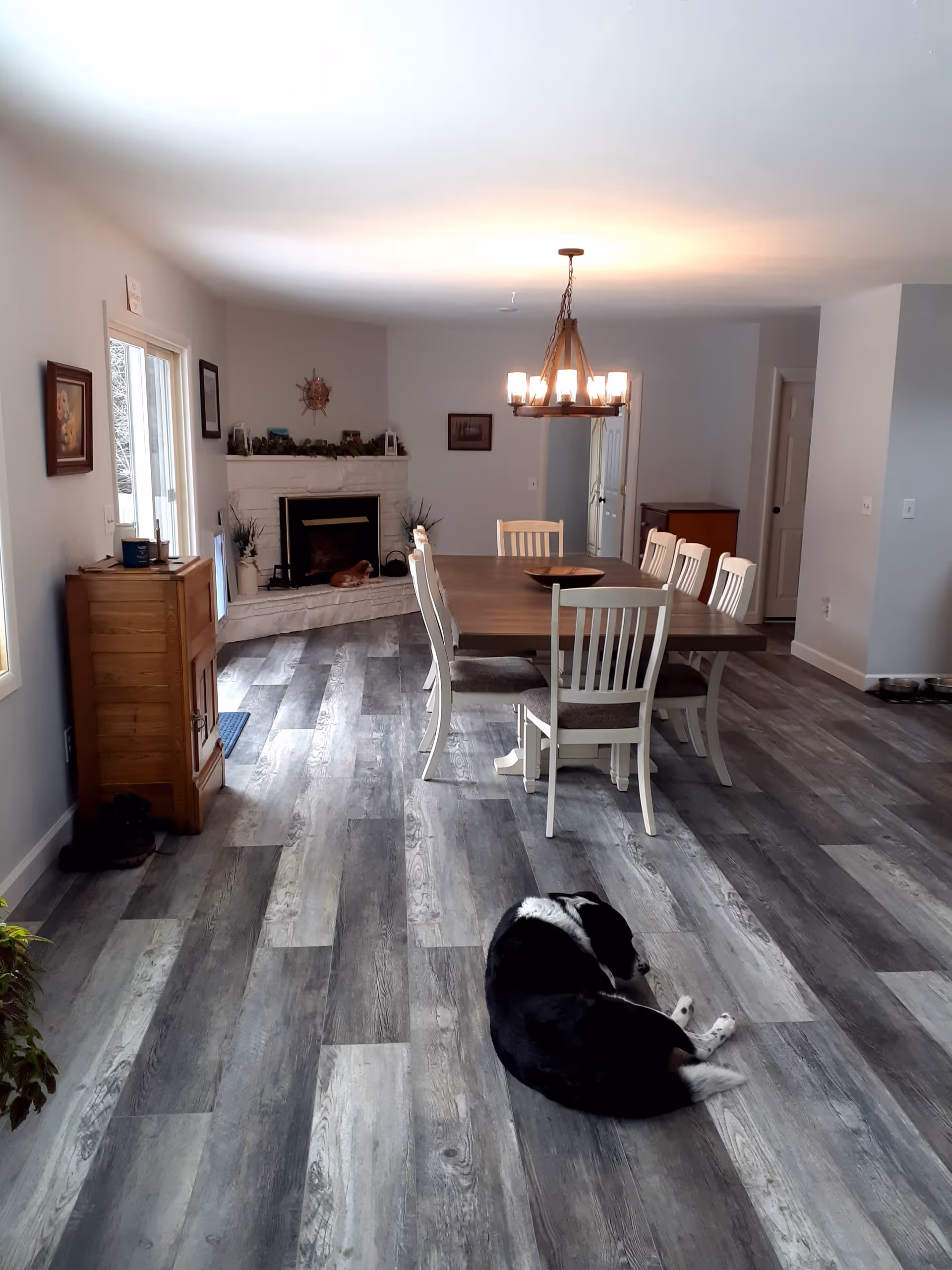Spacious dining room with large table, chandelier, fireplace, and a dog resting.