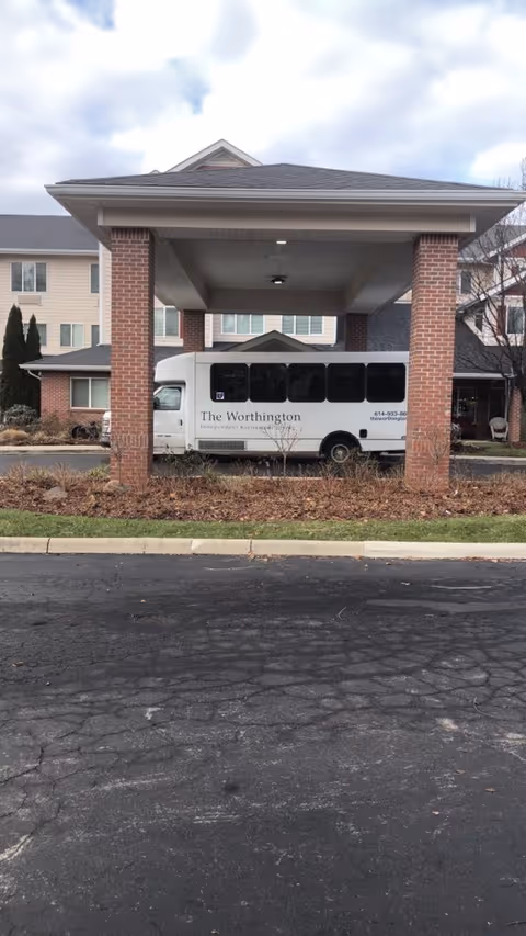 Senior living facility entrance with a white shuttle bus parked under a covered porte-cochere.