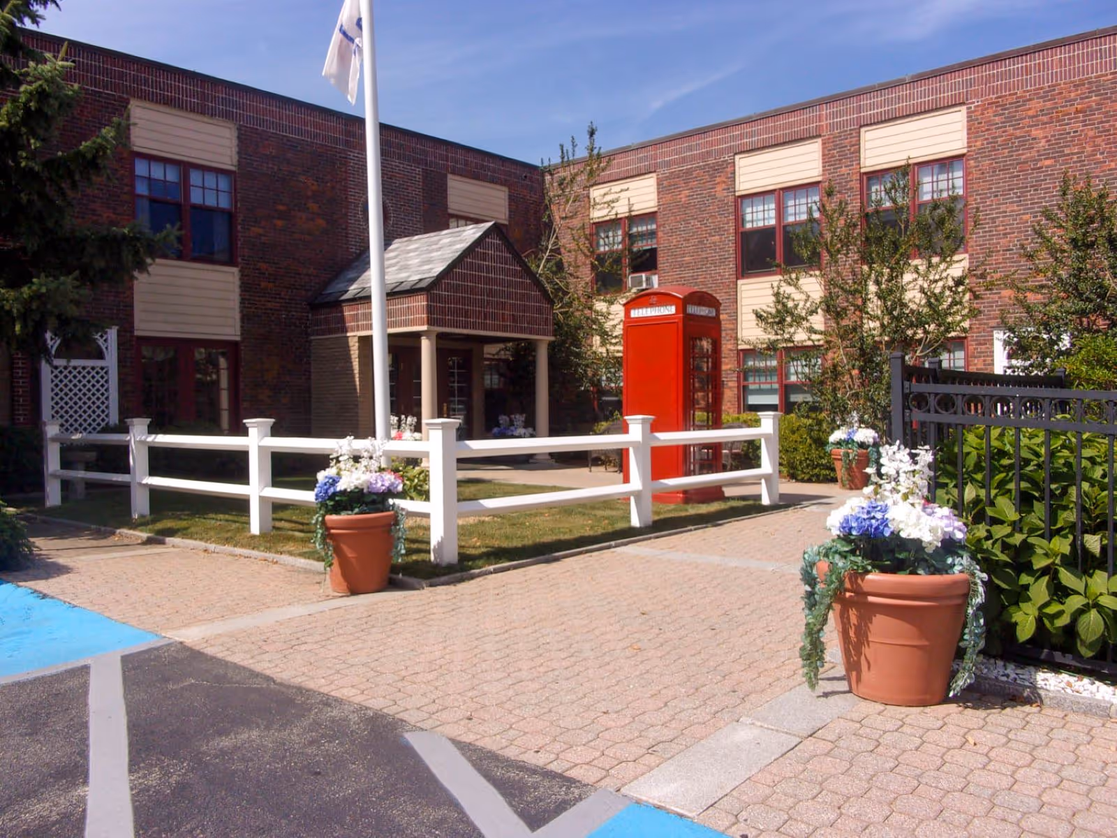 Exterior view of Brandon Woods of Dartmouth with brick building, white fence, and potted flowers.