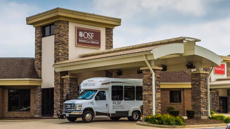 A white OSF medical van parked in front of a stone-clad building.