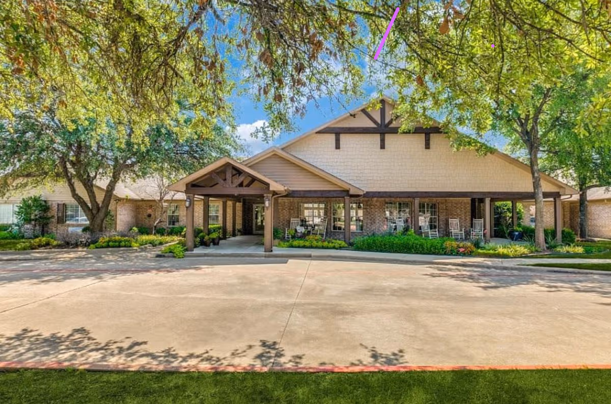 Front view of a brick senior living facility with a covered entrance and rocking chairs.